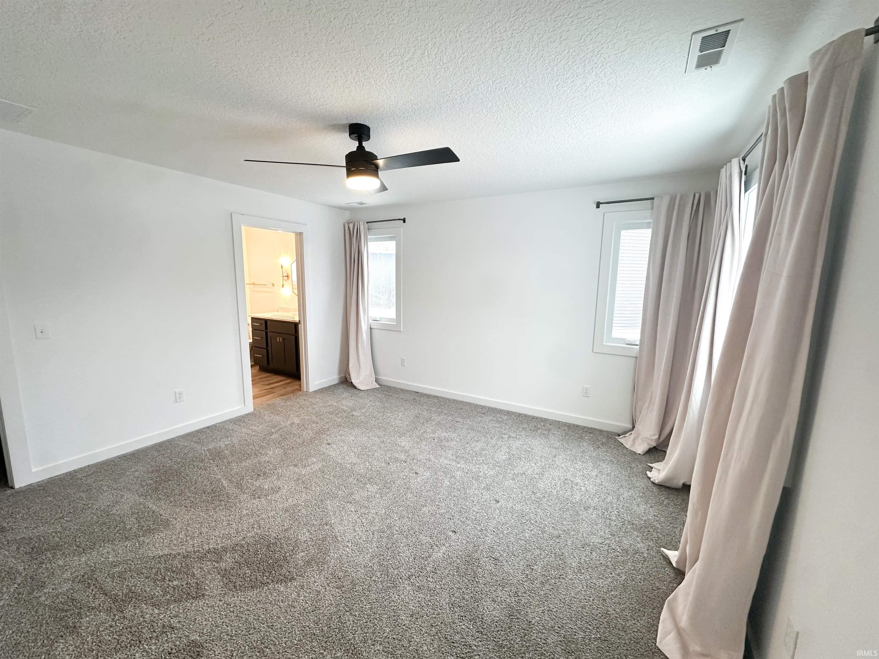 Unfurnished bedroom with a textured ceiling, a ceiling fan, light carpet, and ensuite bathroom