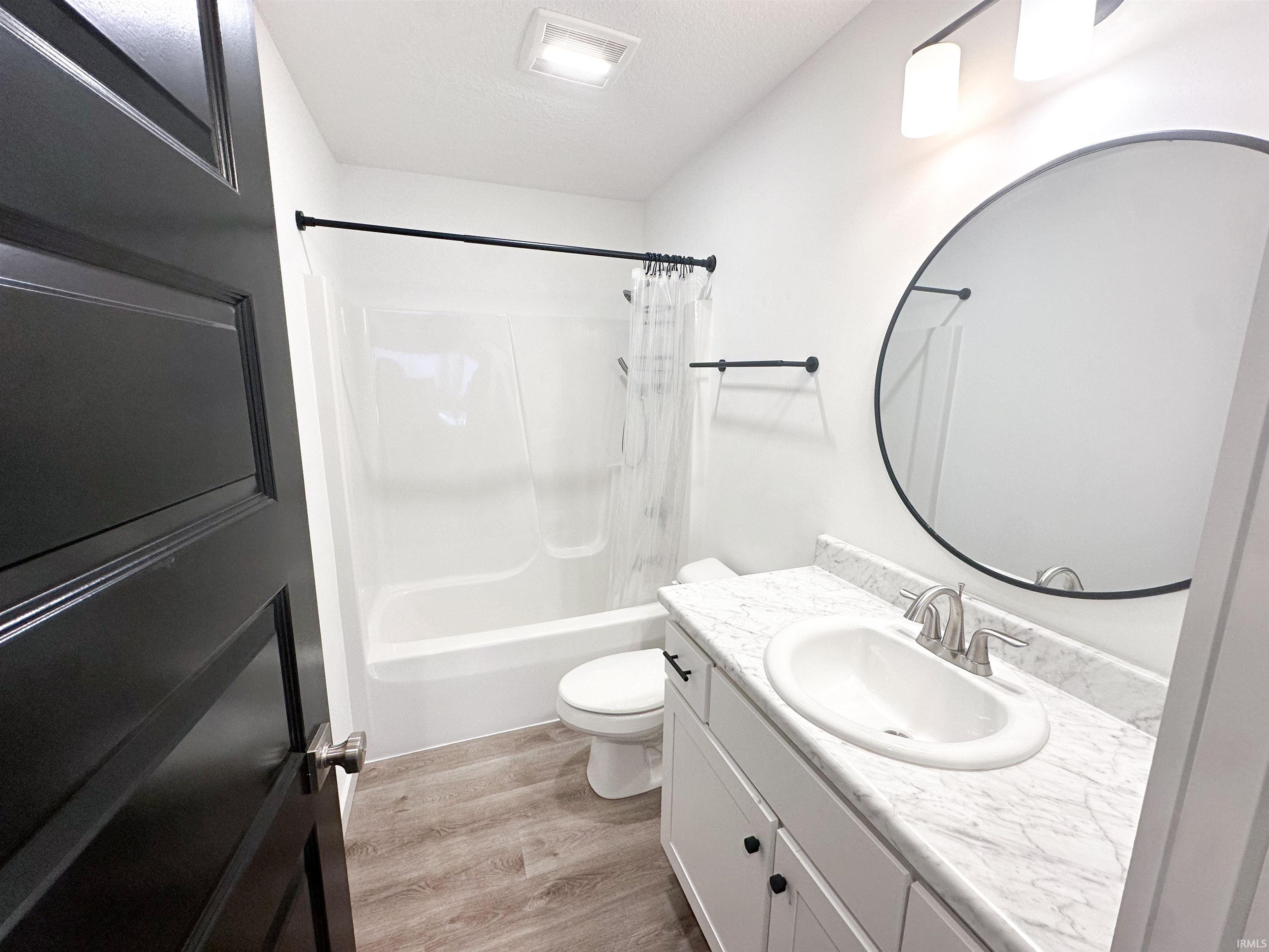 Bathroom with shower / bathtub combination with curtain, vanity, light wood finished floors, and a textured ceiling