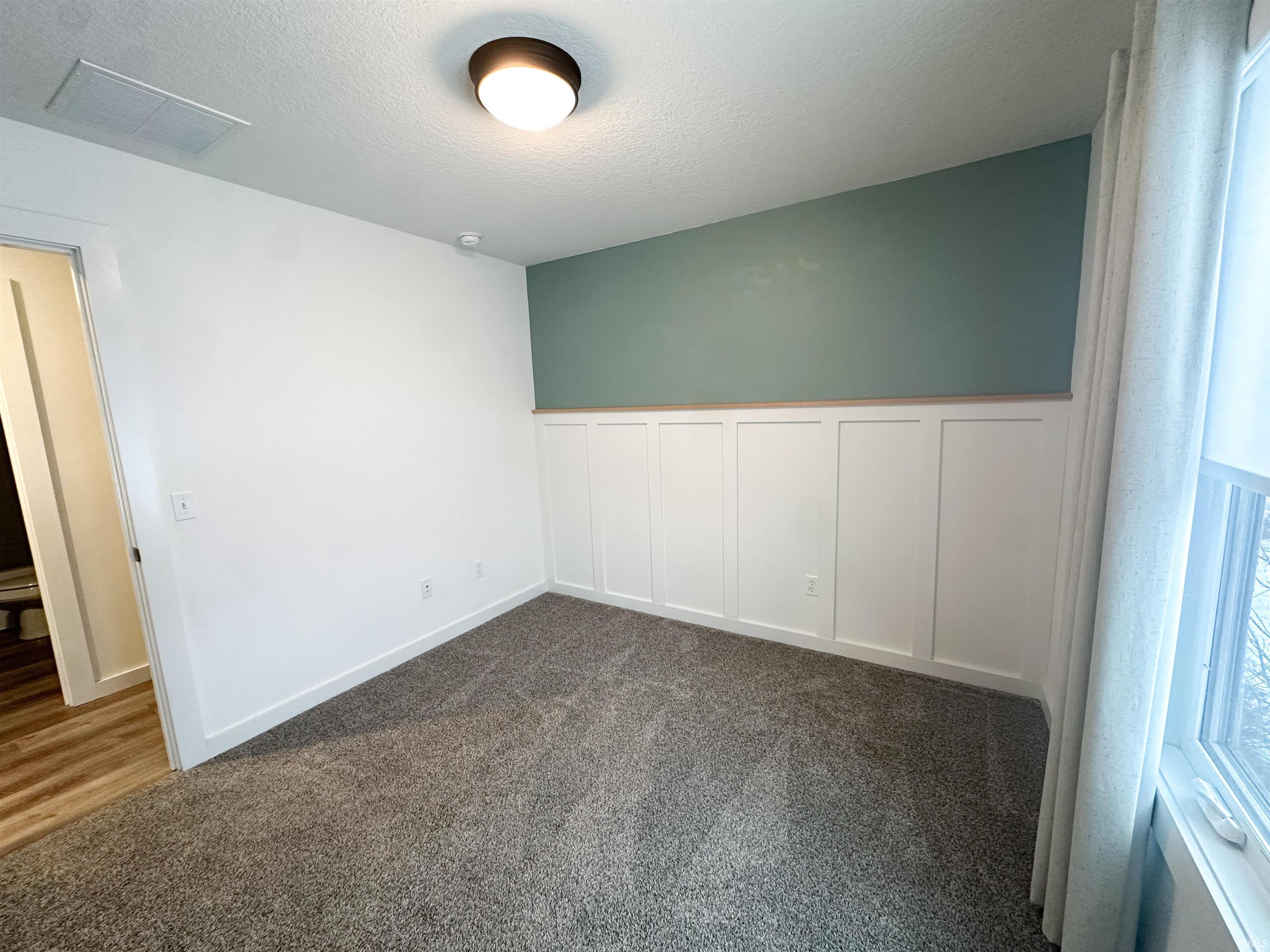 Bedroom featuring a decorative wall, a wainscoted wall, dark colored carpet, and a textured ceiling