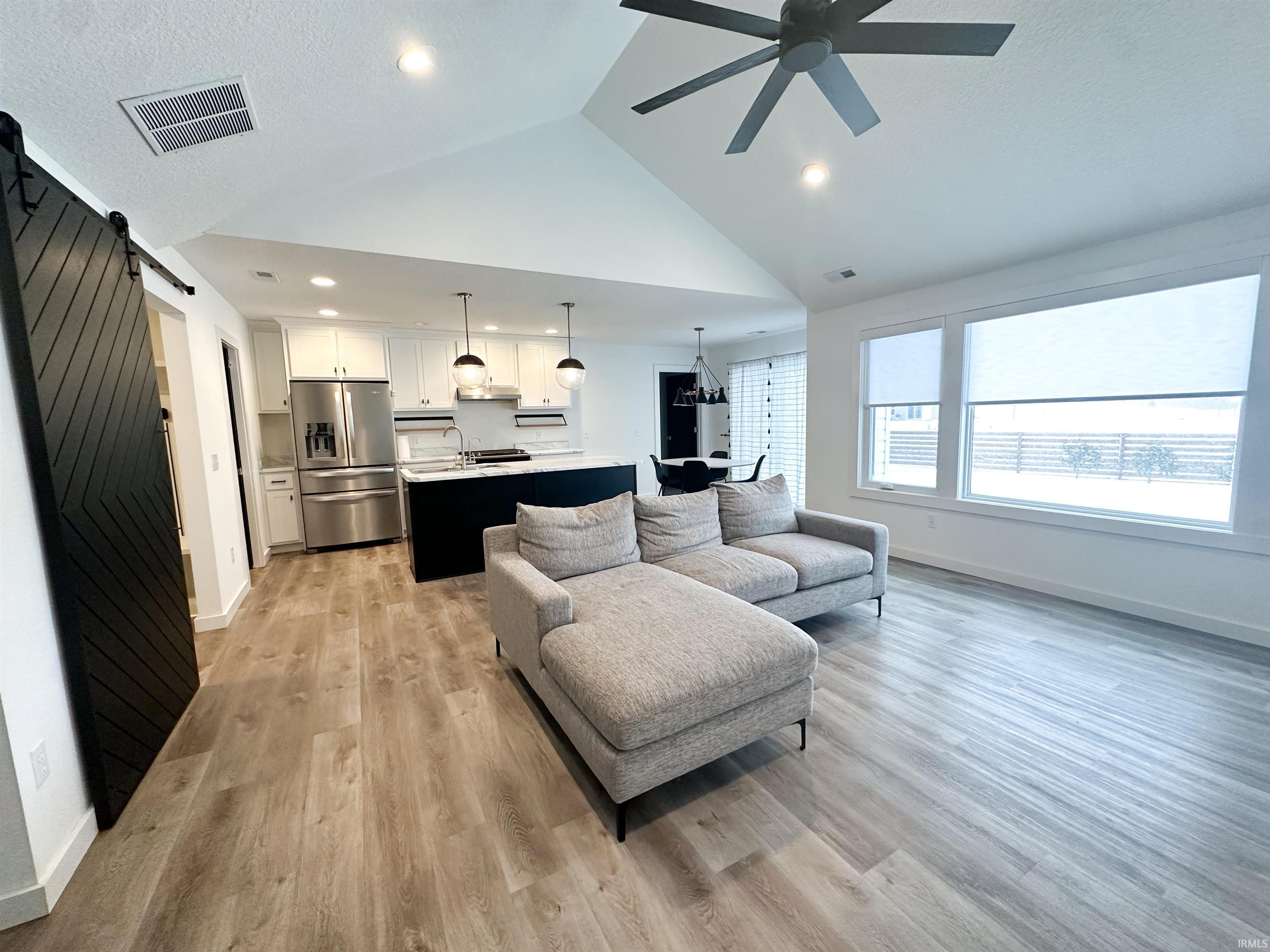 Living room featuring a barn door, light wood-style flooring, a ceiling fan, a textured ceiling, and high vaulted ceiling