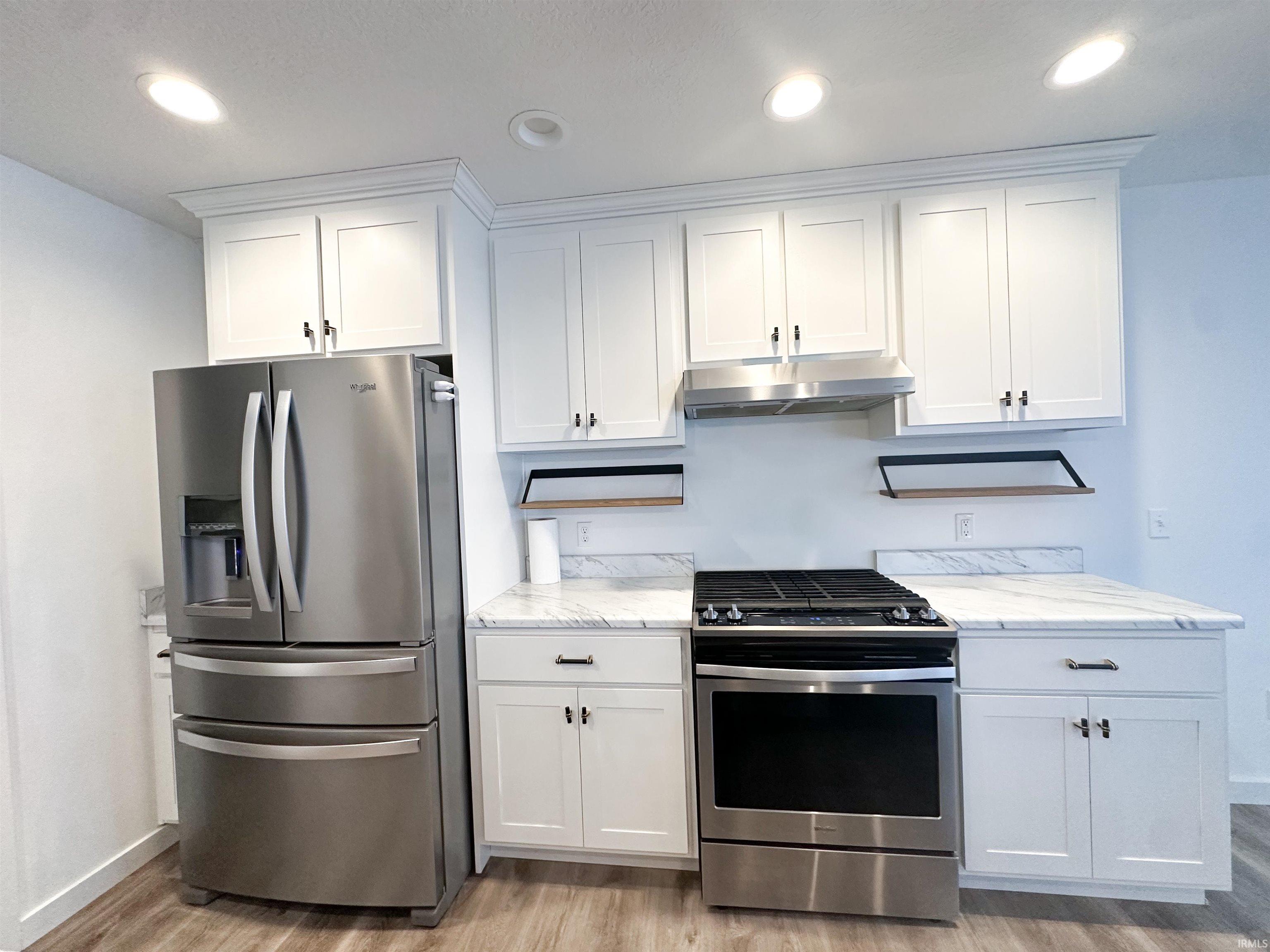 Kitchen with appliances with stainless steel finishes, white cabinets, under cabinet range hood, light wood-style flooring, and recessed lighting