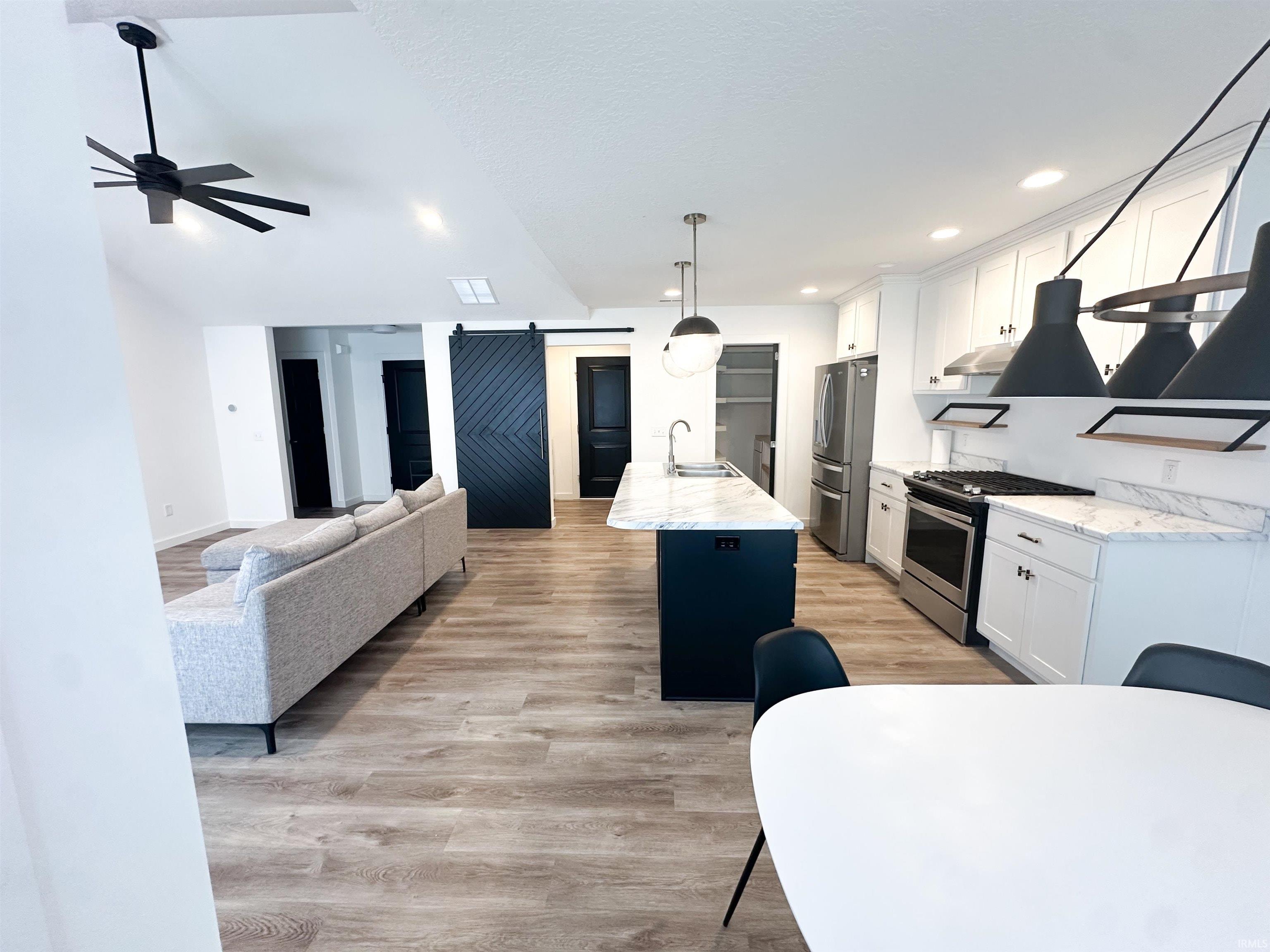 Kitchen featuring a barn door, white cabinetry, stainless steel appliances, hanging light fixtures, and recessed lighting