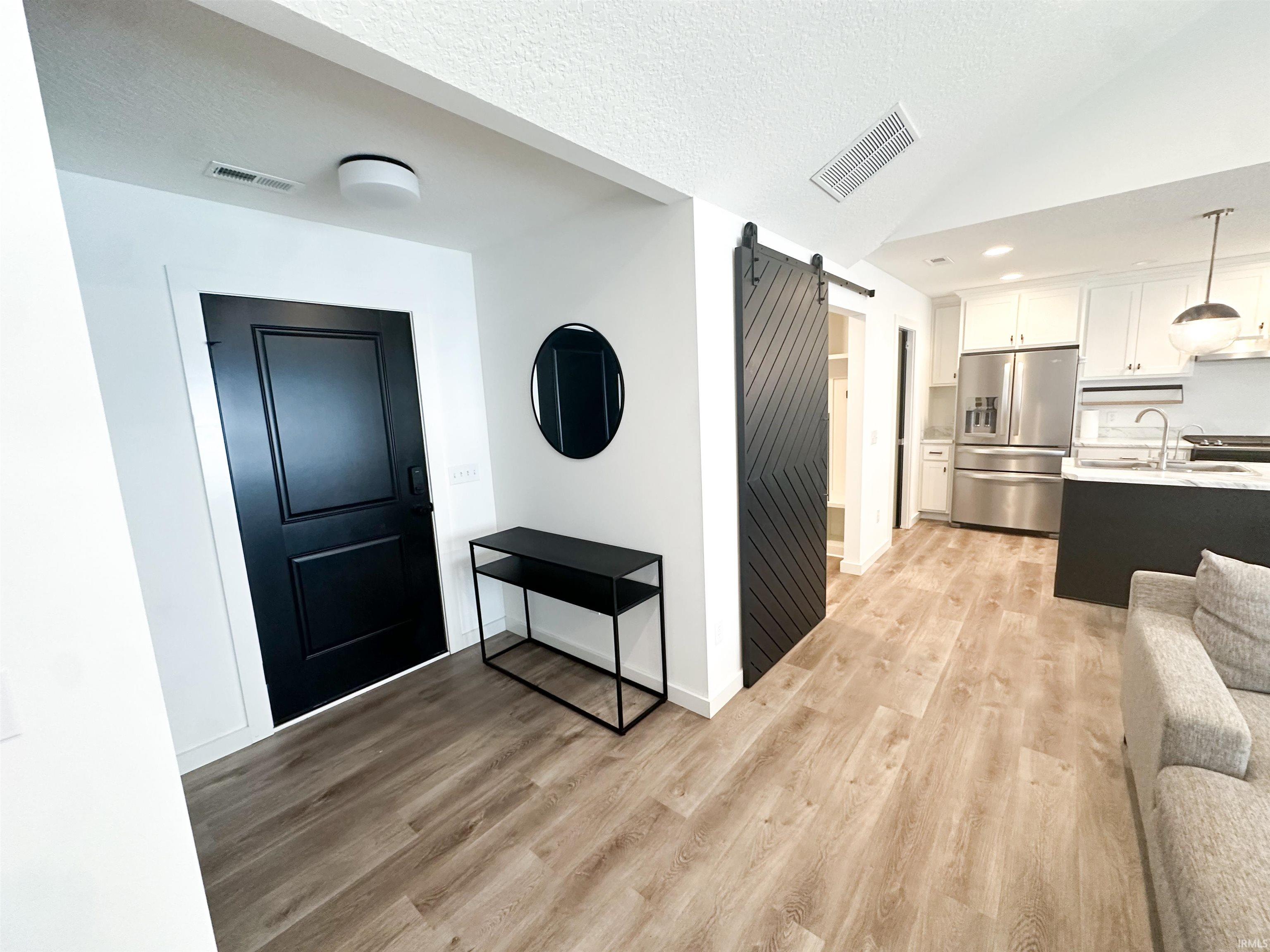 Foyer entrance with a barn door, lofted ceiling, light wood finished floors, a textured ceiling, and recessed lighting