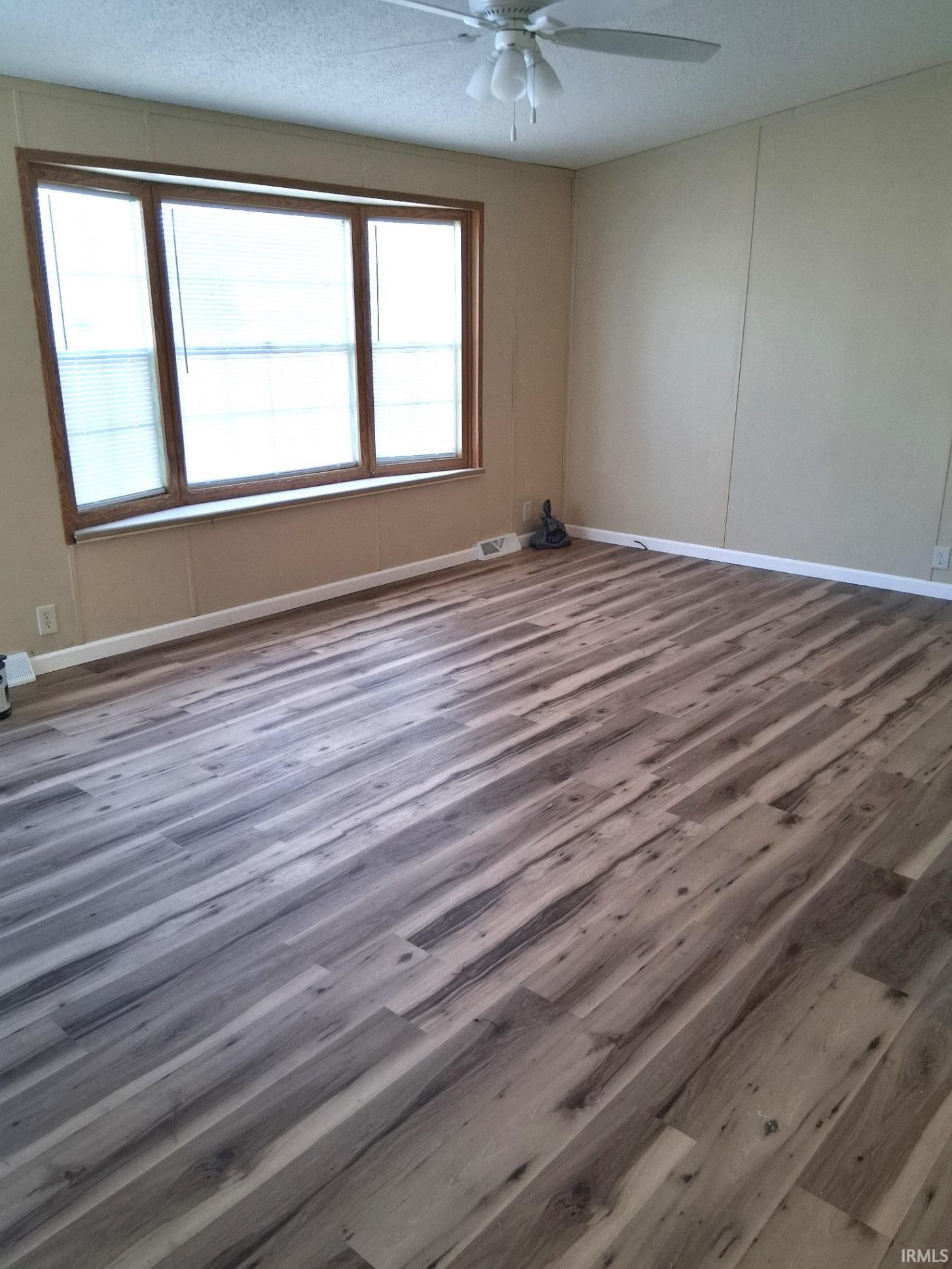 Empty room featuring a textured ceiling, vinyl plank floors, new miniblinds and ceiling fan