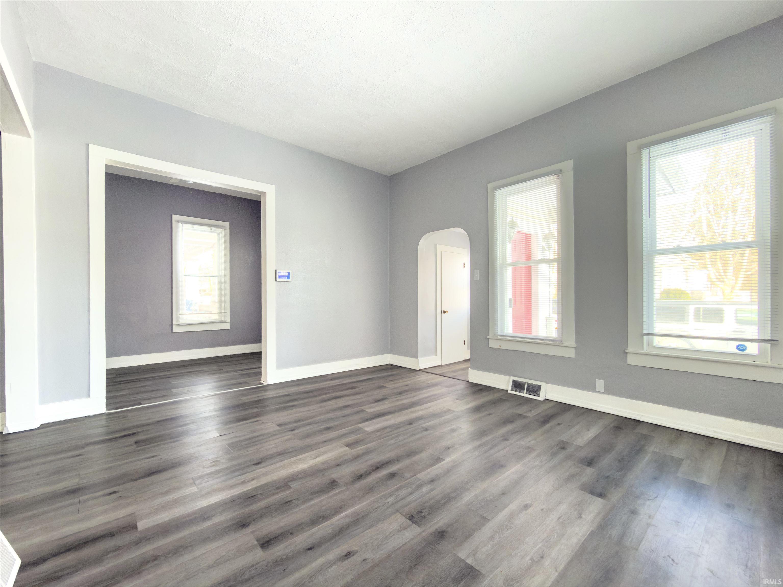 Spare room with healthy amount of natural light, arched walkways, and dark wood finished floors