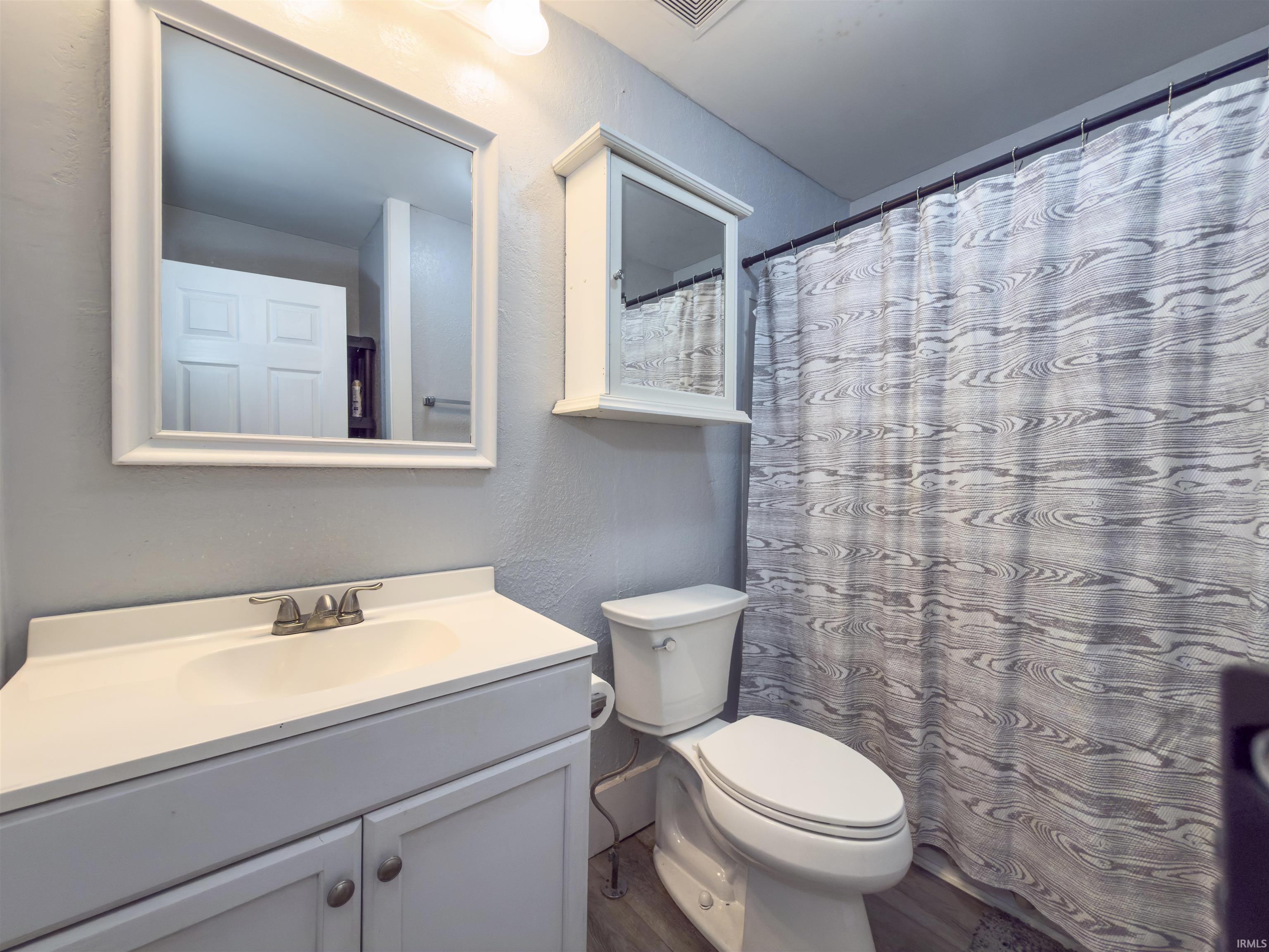 Full bath with curtained shower, vanity, a textured wall, and wood finished floors