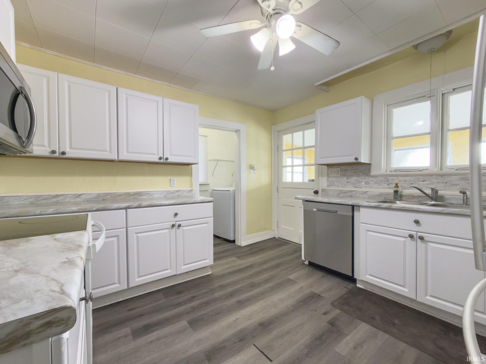 Kitchen with white cabinets, ceiling fan, stainless steel appliances, dark wood-type flooring, and washer / dryer