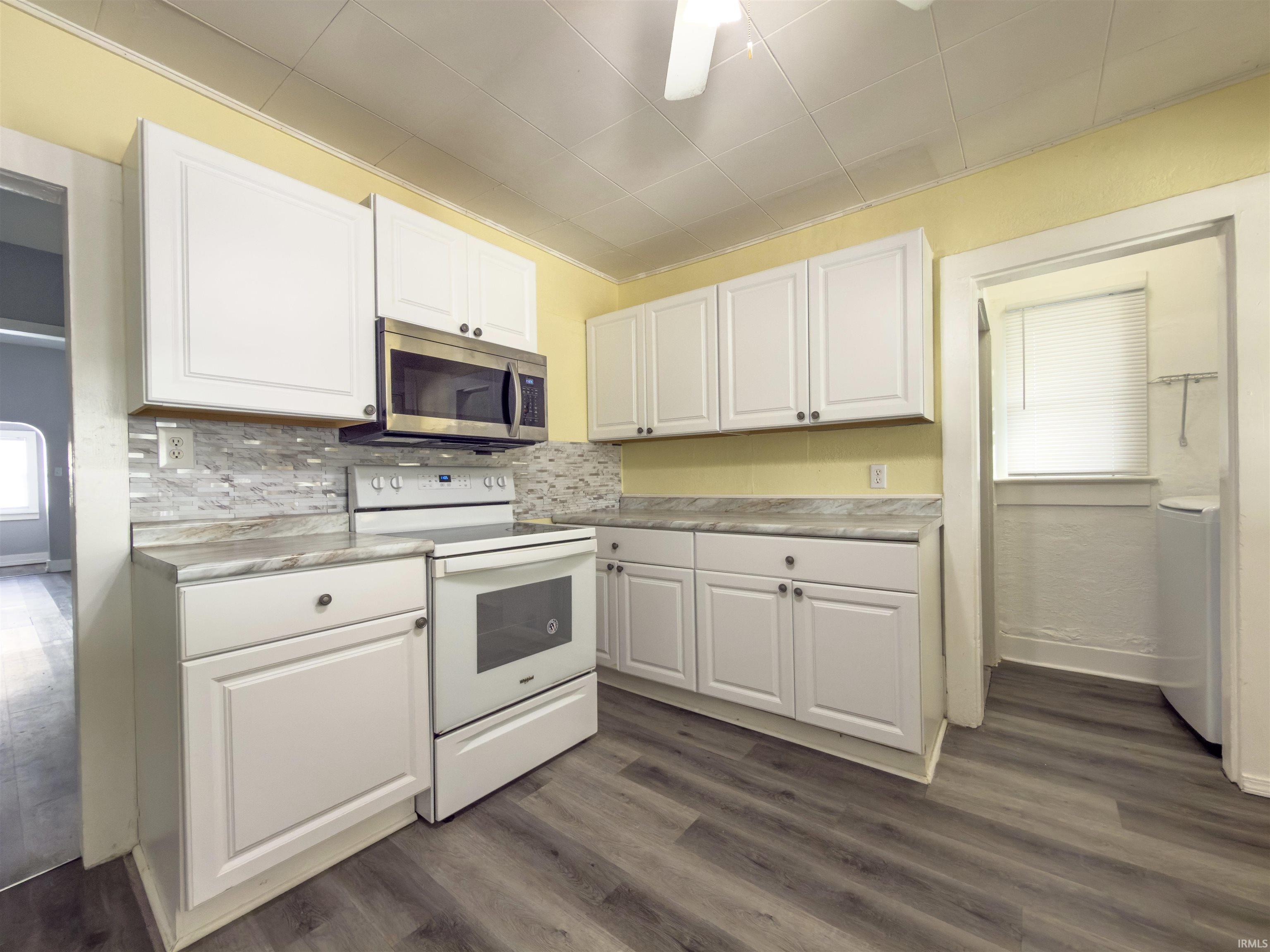 Kitchen featuring white electric range oven, white cabinets, light countertops, stainless steel microwave, and dark wood-style flooring