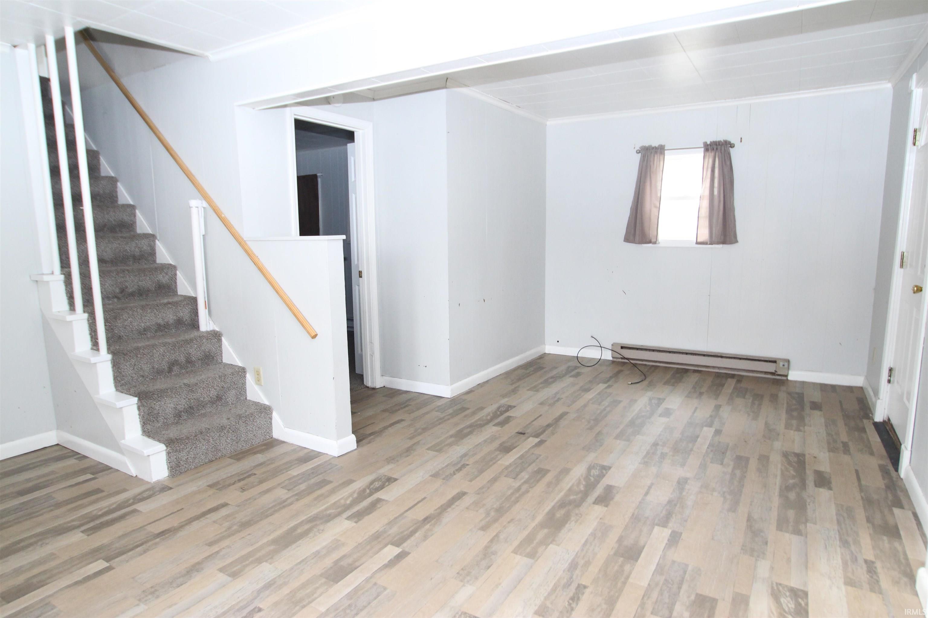 Below grade area featuring light wood-style flooring, a baseboard radiator, and stairs