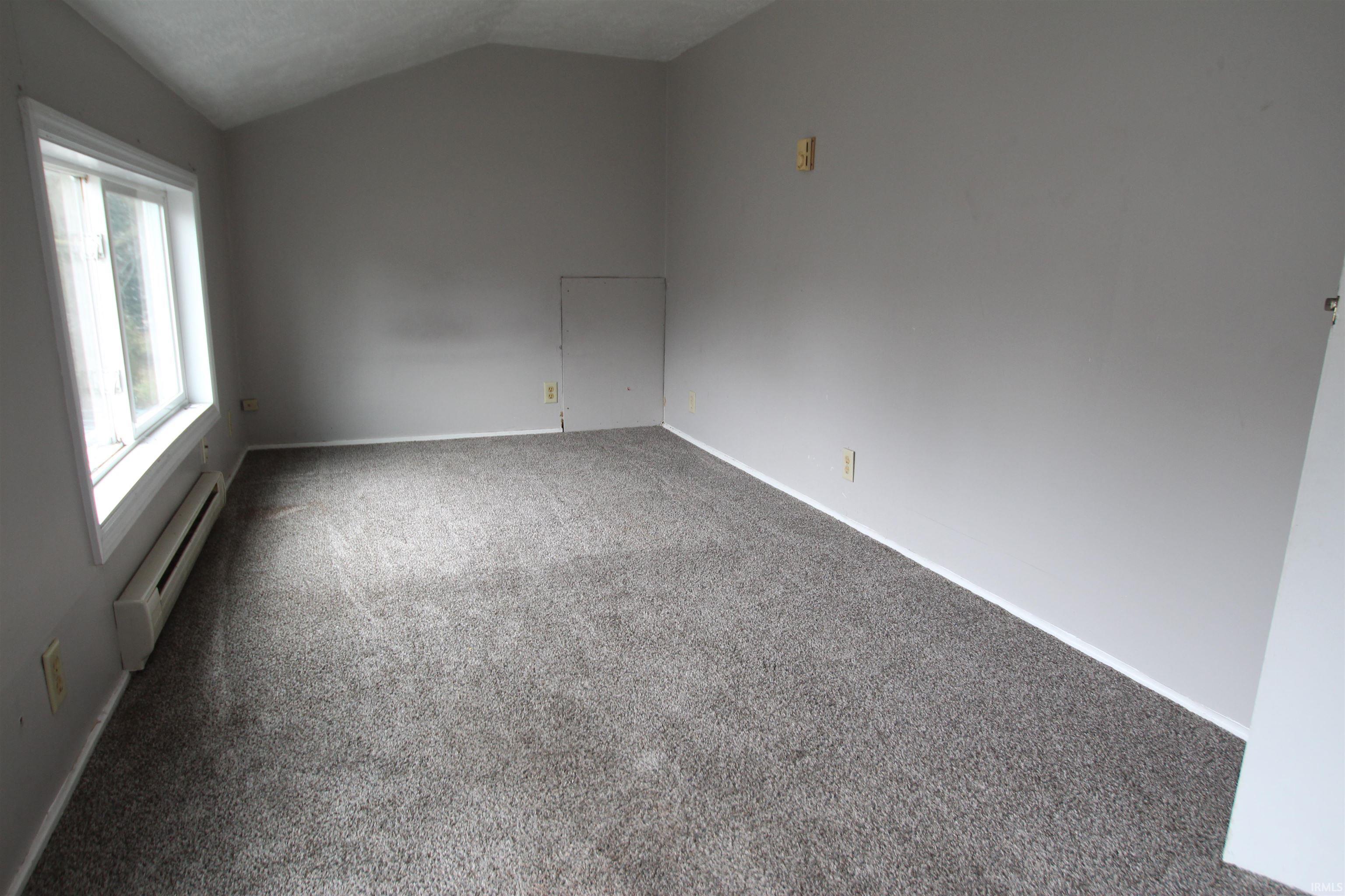 Carpeted spare room featuring a baseboard radiator and vaulted ceiling