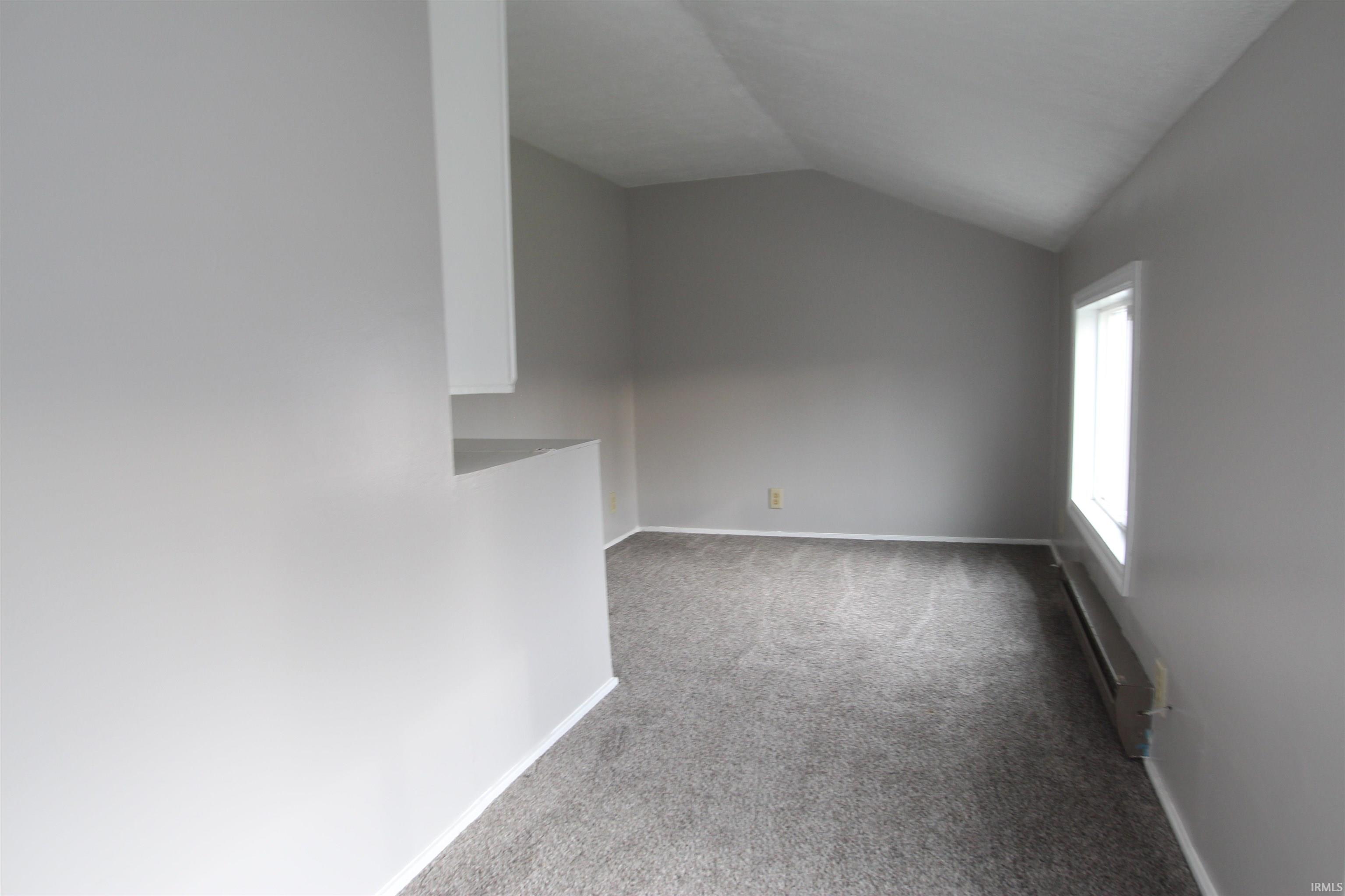 Unfurnished room with light colored carpet, lofted ceiling, and a baseboard radiator