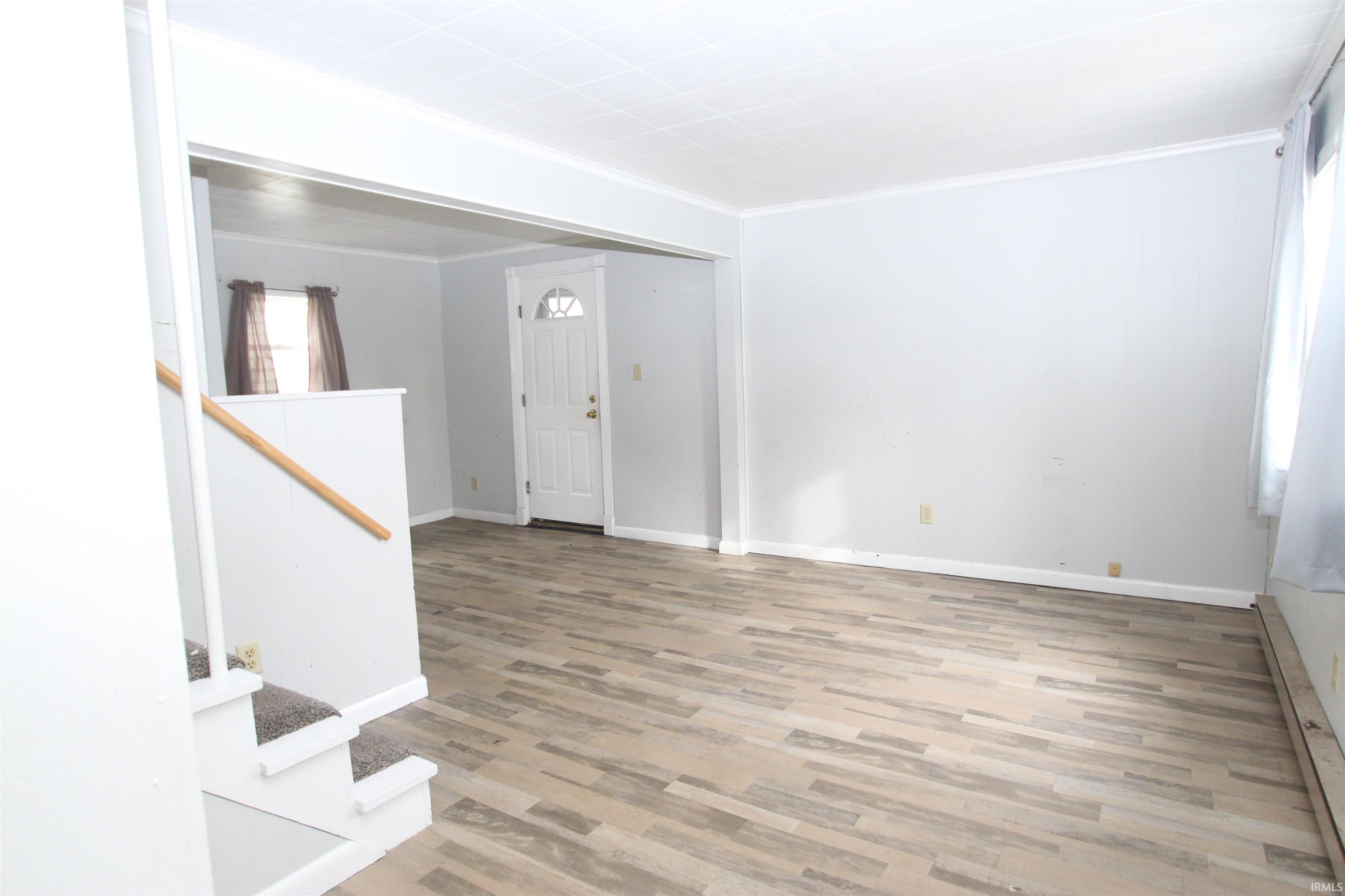 Entryway featuring baseboard heating, light wood finished floors, crown molding, and stairway