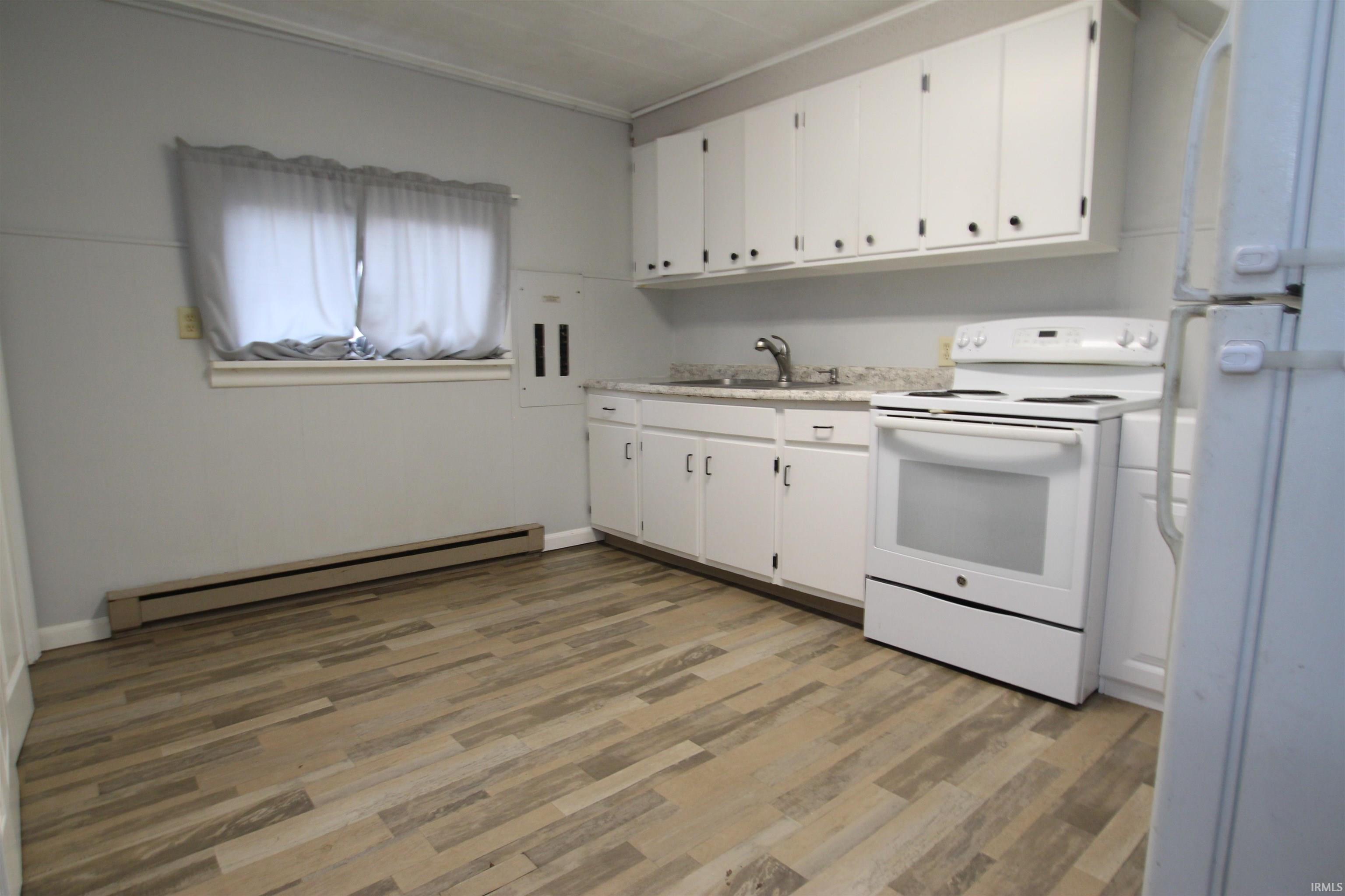 Kitchen featuring white appliances, light countertops, a baseboard radiator, white cabinets, and ornamental molding