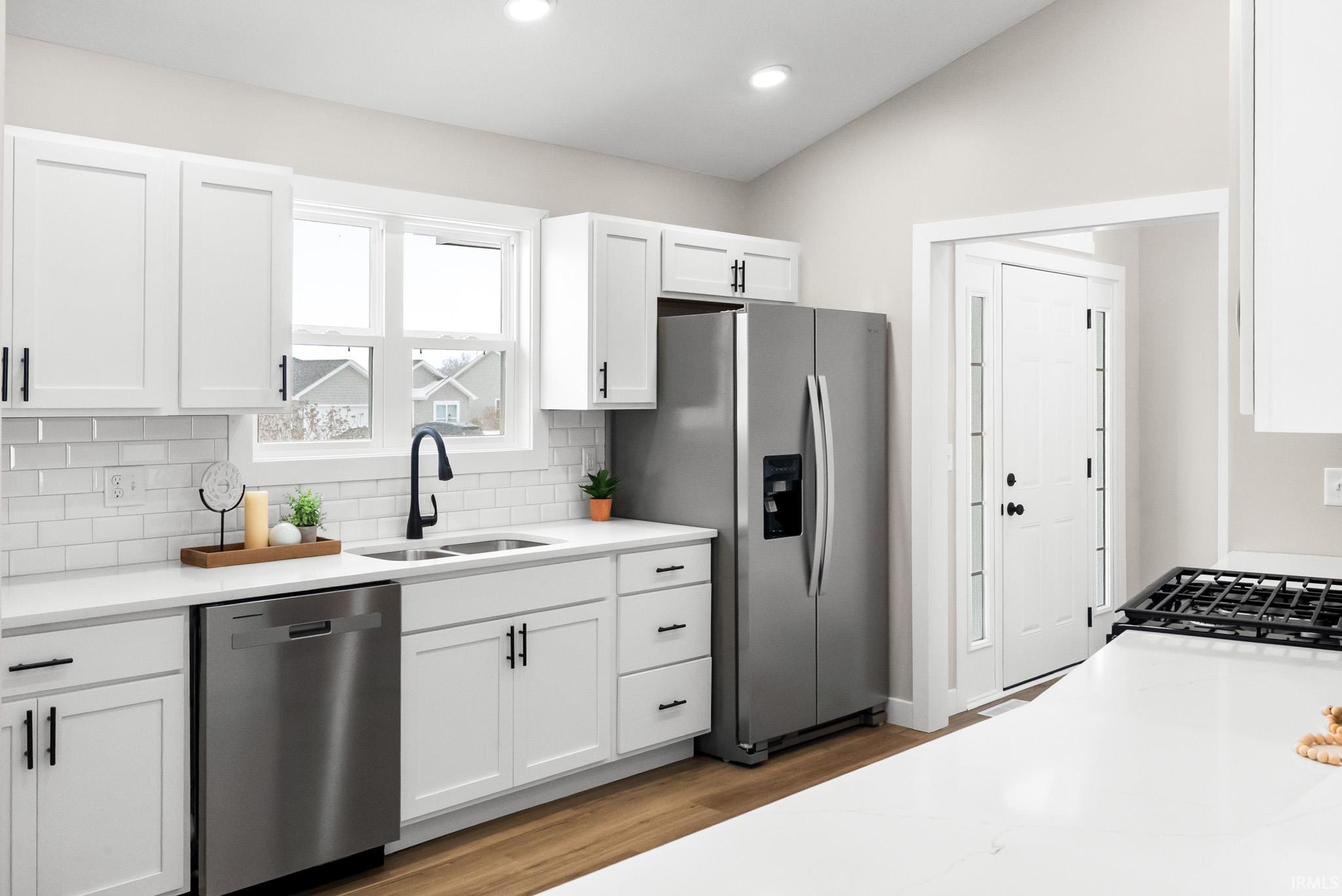 Kitchen featuring appliances with stainless steel finishes, white cabinetry, light wood-type flooring, vaulted ceiling, and light stone countertops