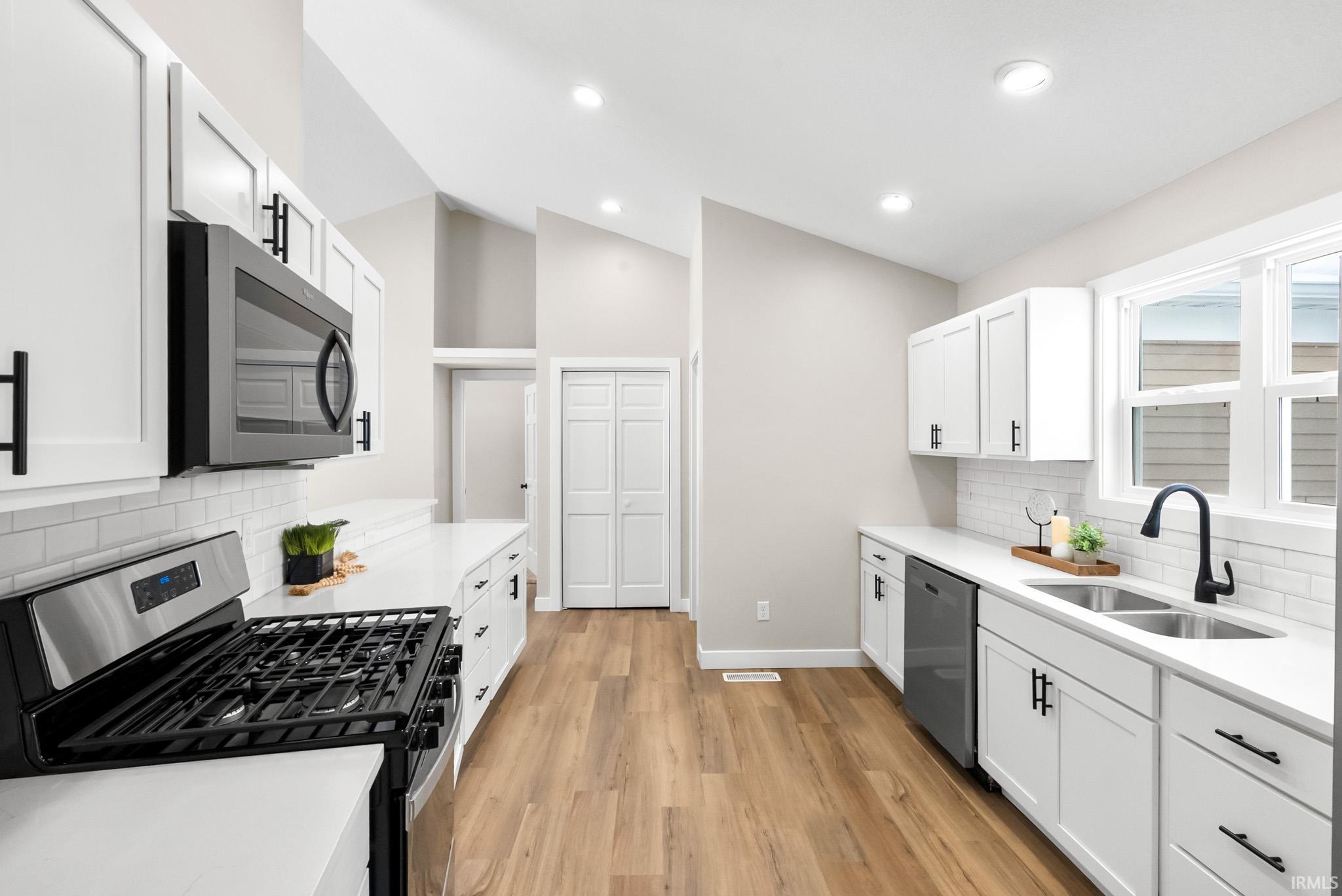 Kitchen with backsplash, appliances with stainless steel finishes, white cabinets, vaulted ceiling, and light stone countertops