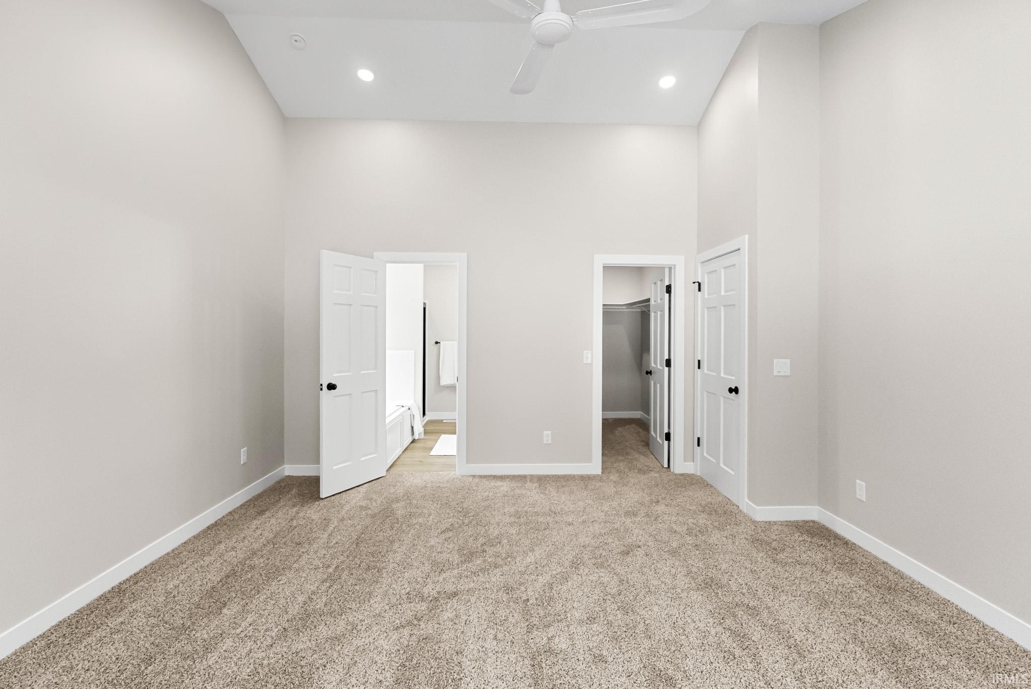 Unfurnished bedroom featuring a towering ceiling, a walk in closet, ensuite bathroom, light colored carpet, and a ceiling fan