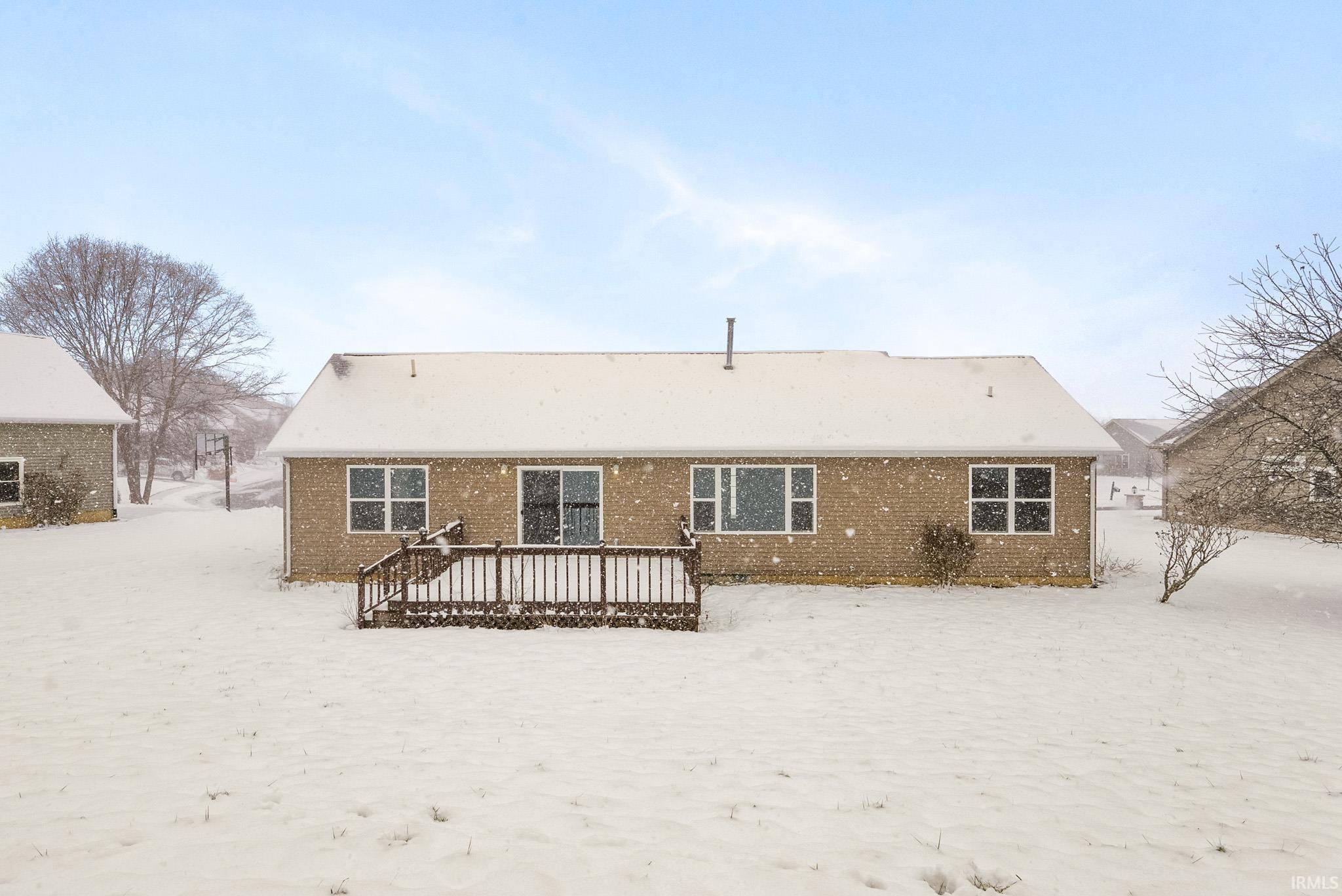 Snow covered rear of property featuring a deck and brick siding