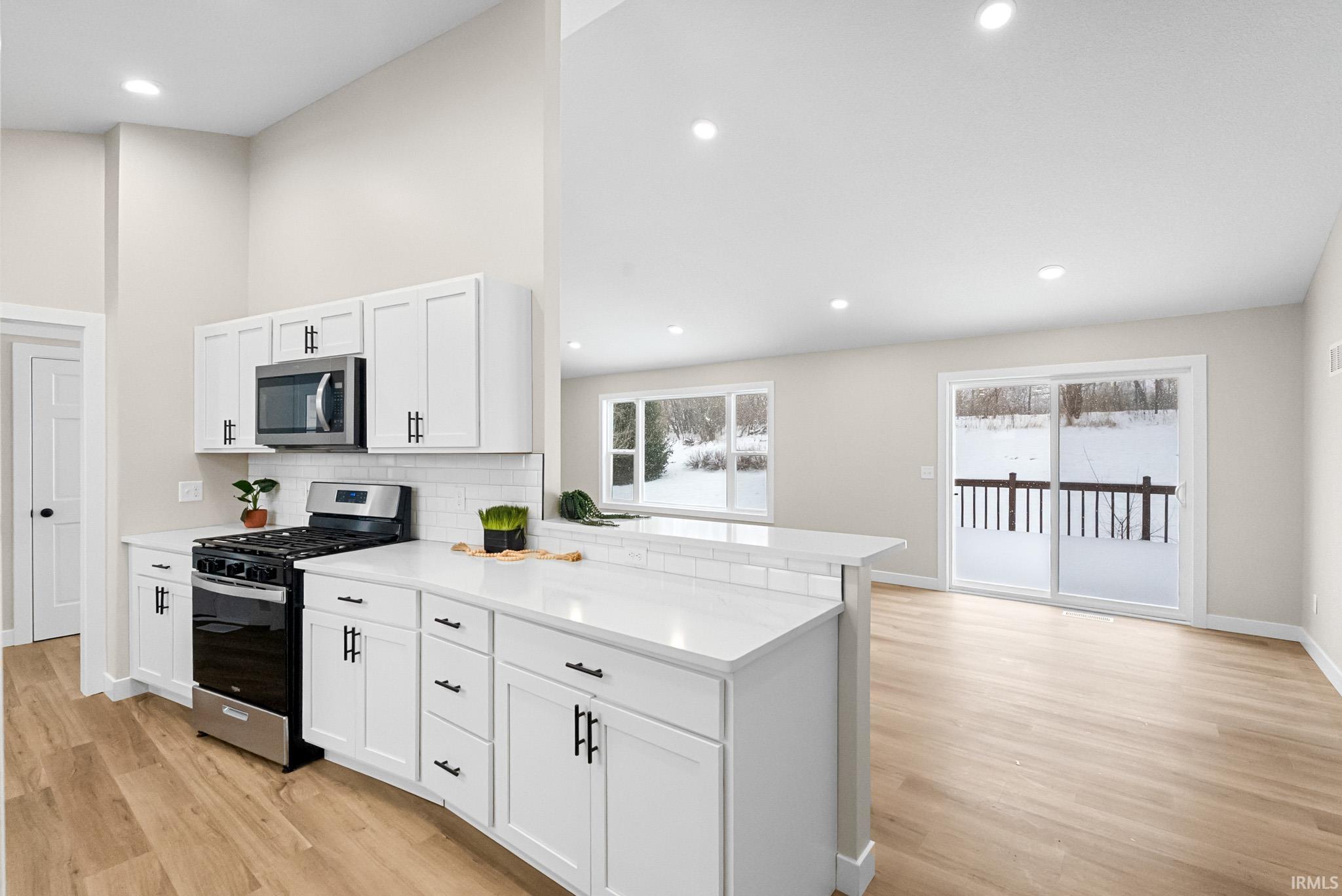 Kitchen with stainless steel appliances, light wood-style flooring, white cabinetry, high vaulted ceiling, and decorative backsplash