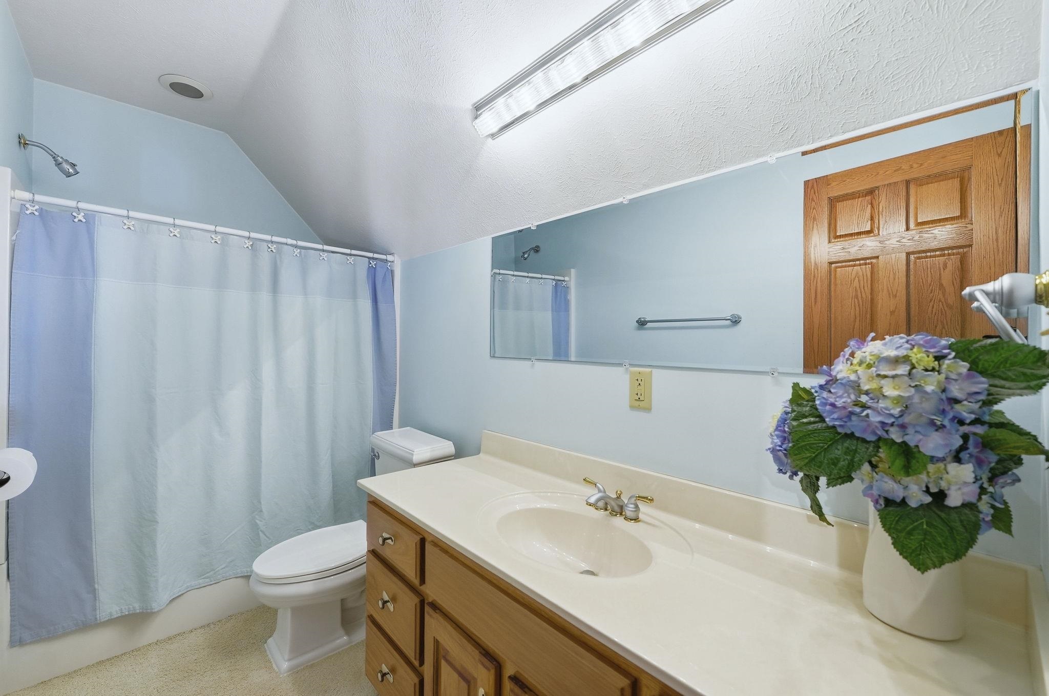 Bathroom featuring vanity, lofted ceiling, shower / bath combo with shower curtain, and a textured ceiling