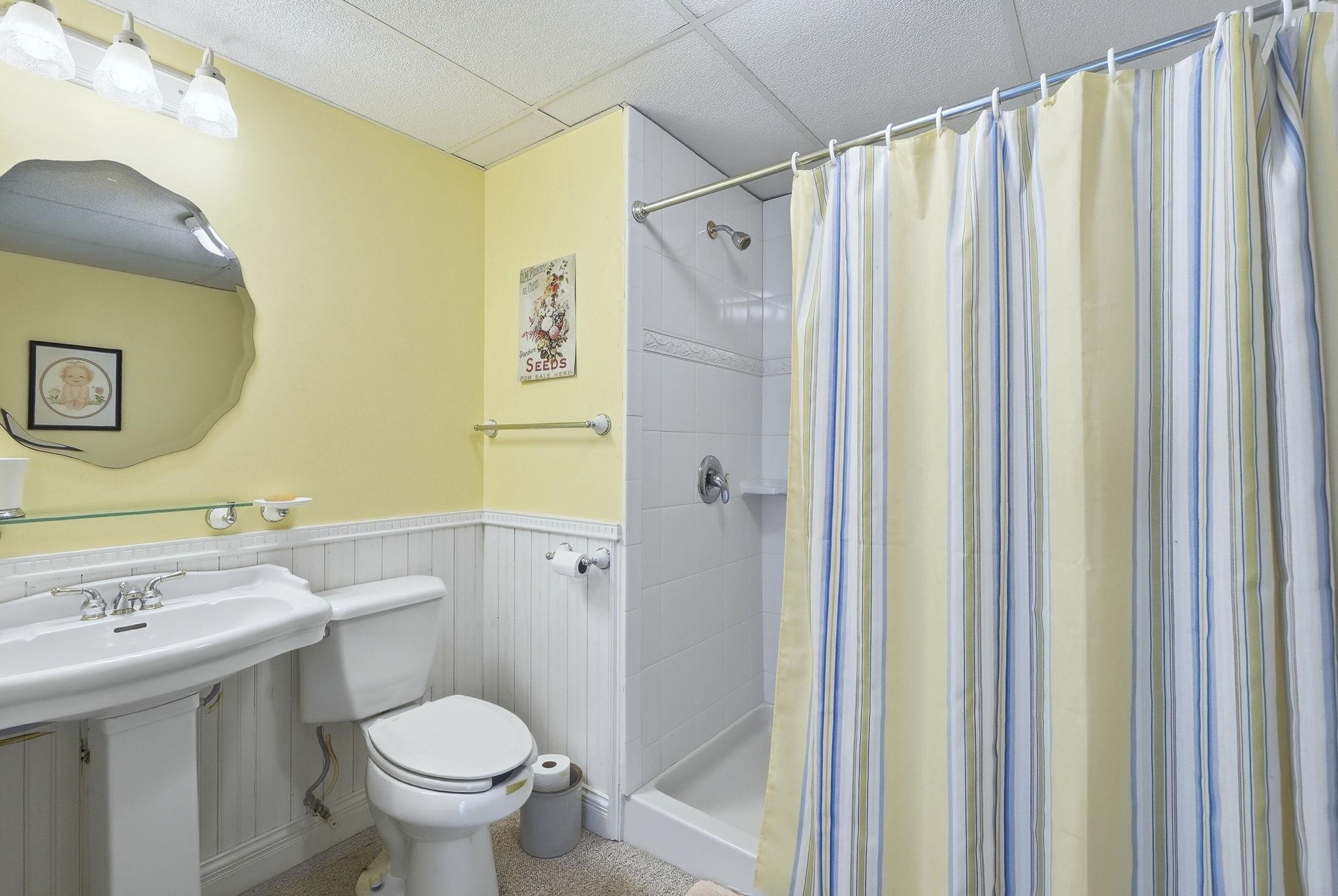 Full bath with a wainscoted wall, a stall shower, and a drop ceiling