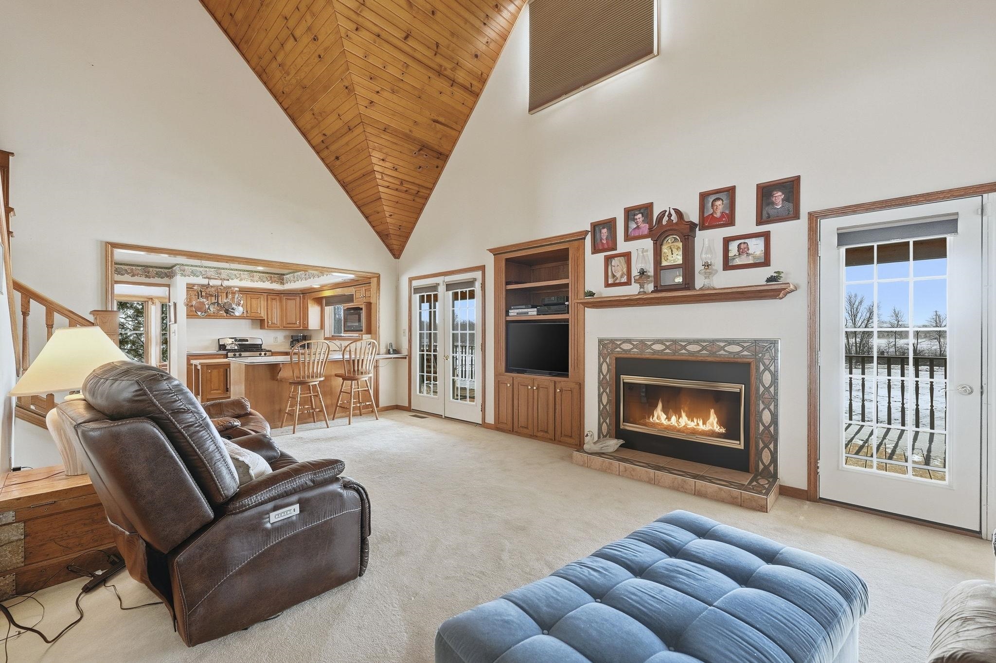 Living area featuring high vaulted ceiling, light carpet, a fireplace, wood ceiling, and built in shelves