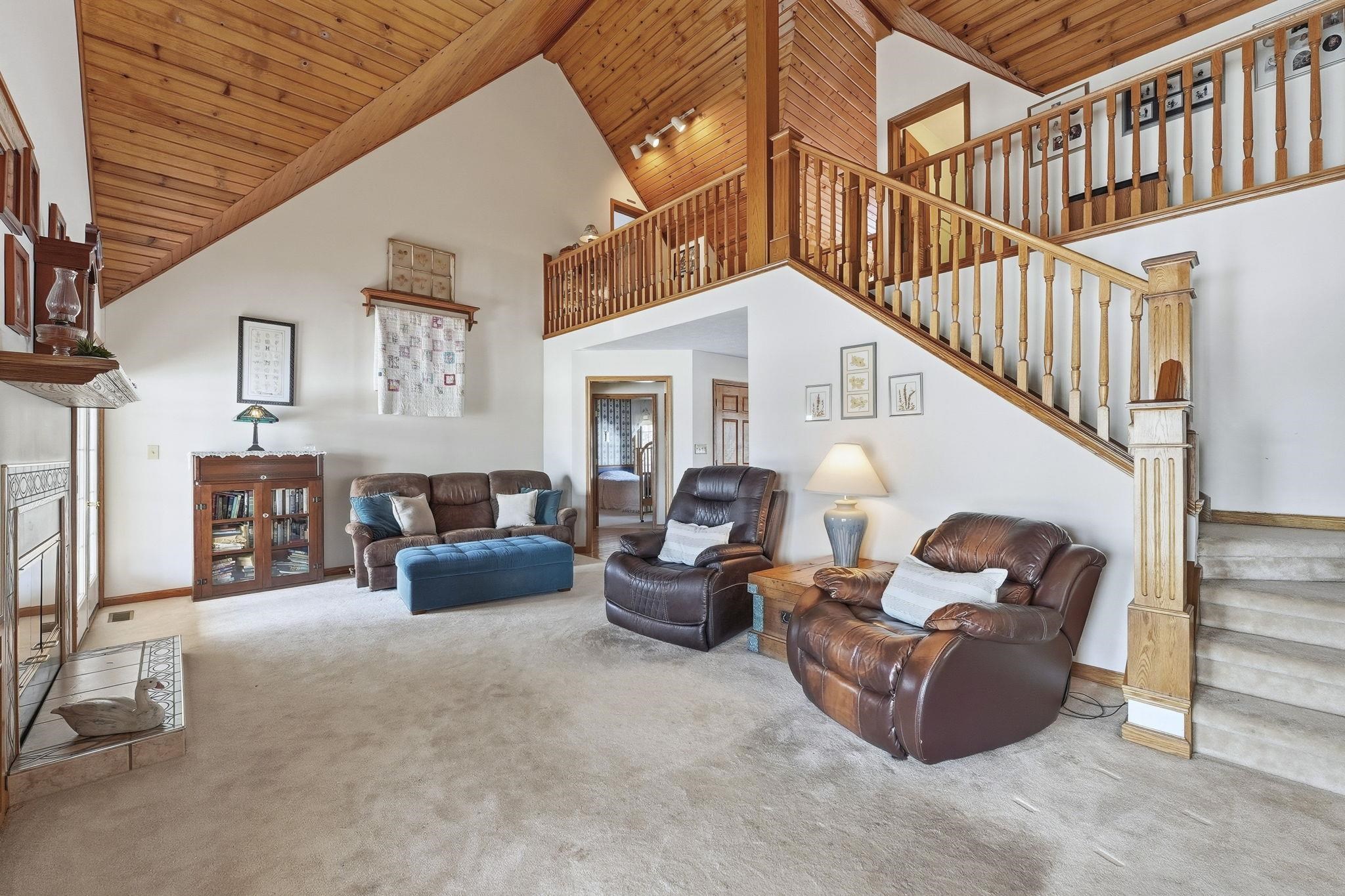 Living area featuring a fireplace, high vaulted ceiling, wood ceiling, carpet floors, and stairs