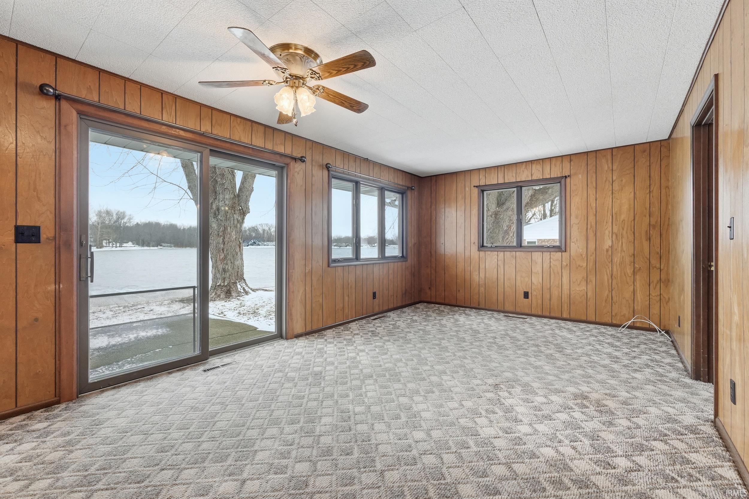 Empty room with wooden walls, a water view, light colored carpet, and a ceiling fan