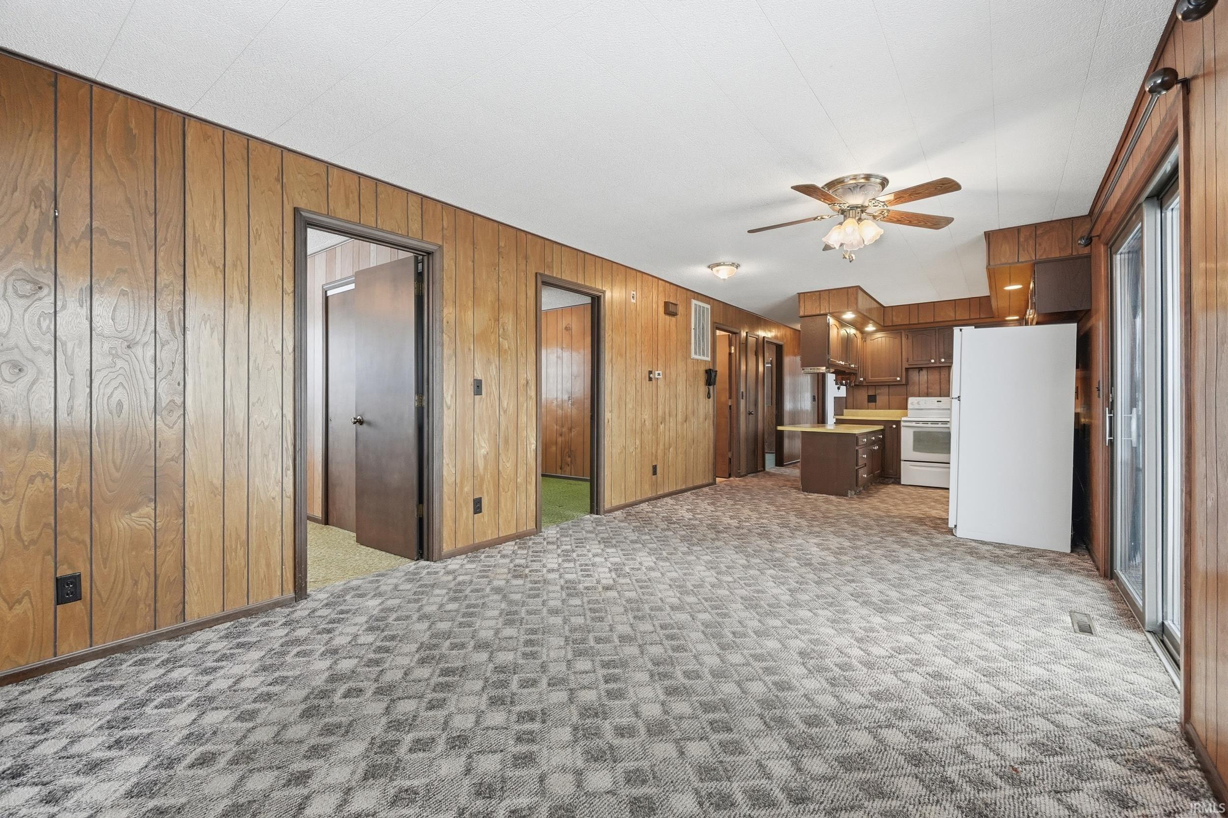 Unfurnished living room featuring wood walls, ceiling fan, and light carpet