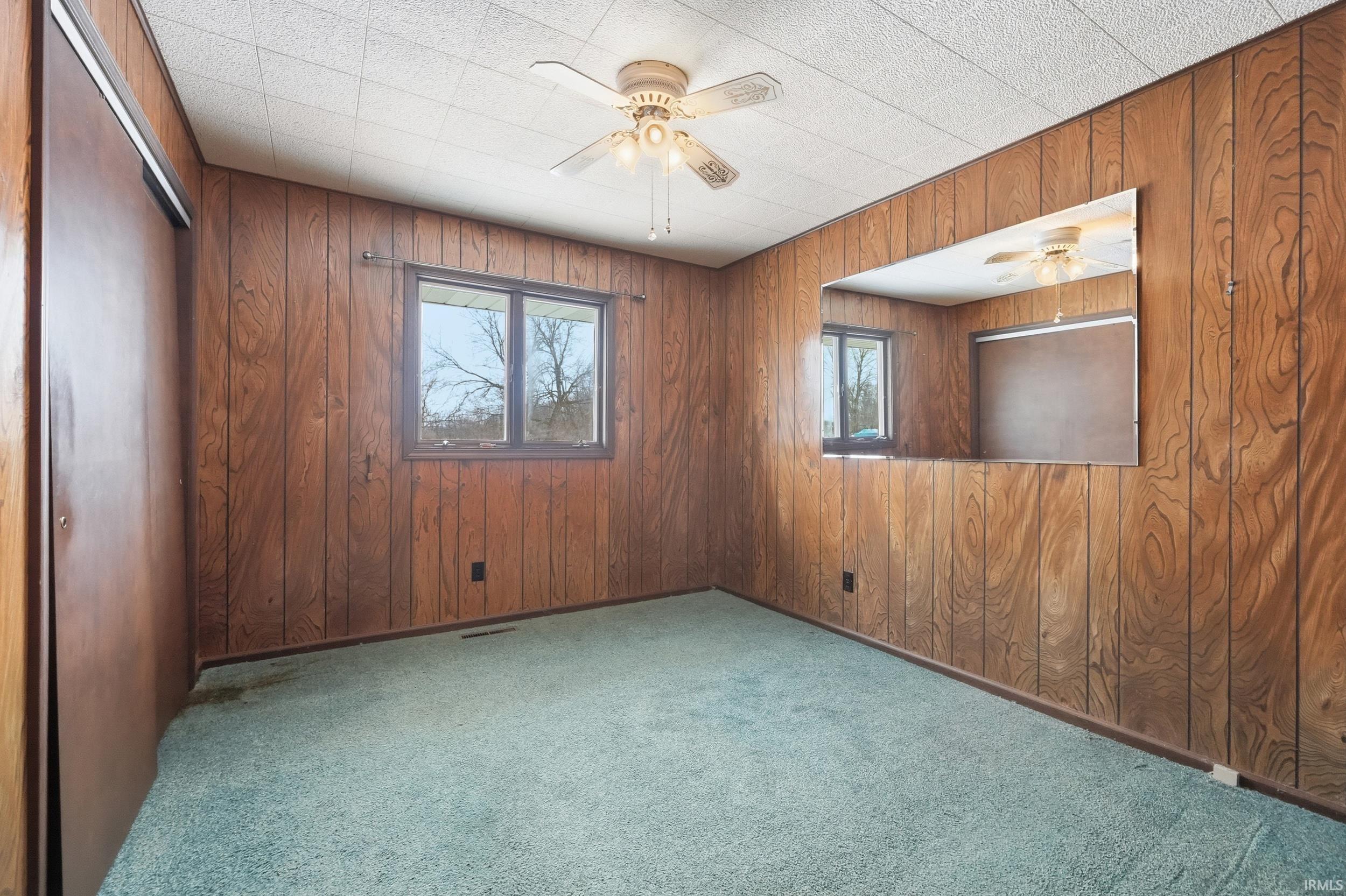 Carpeted empty room with a ceiling fan and wooden walls