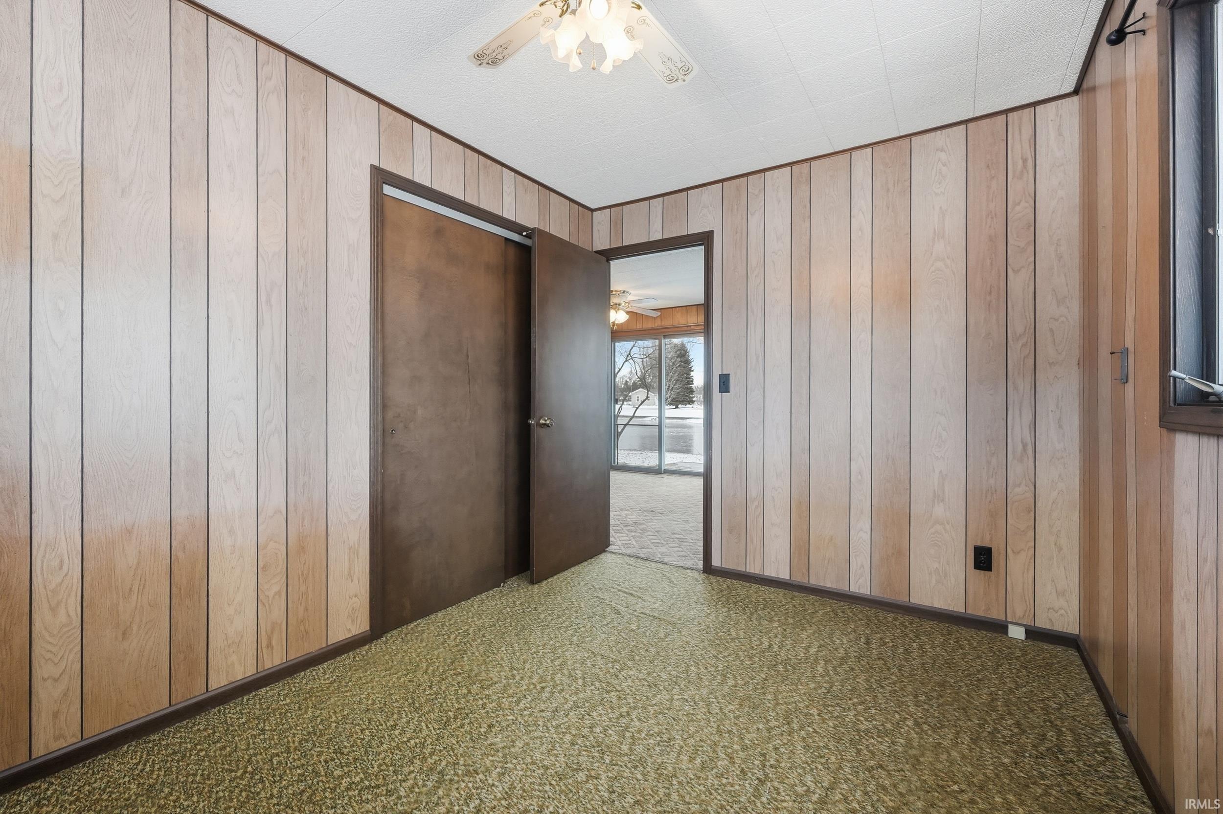Unfurnished room with wood walls, carpet floors, and a ceiling fan