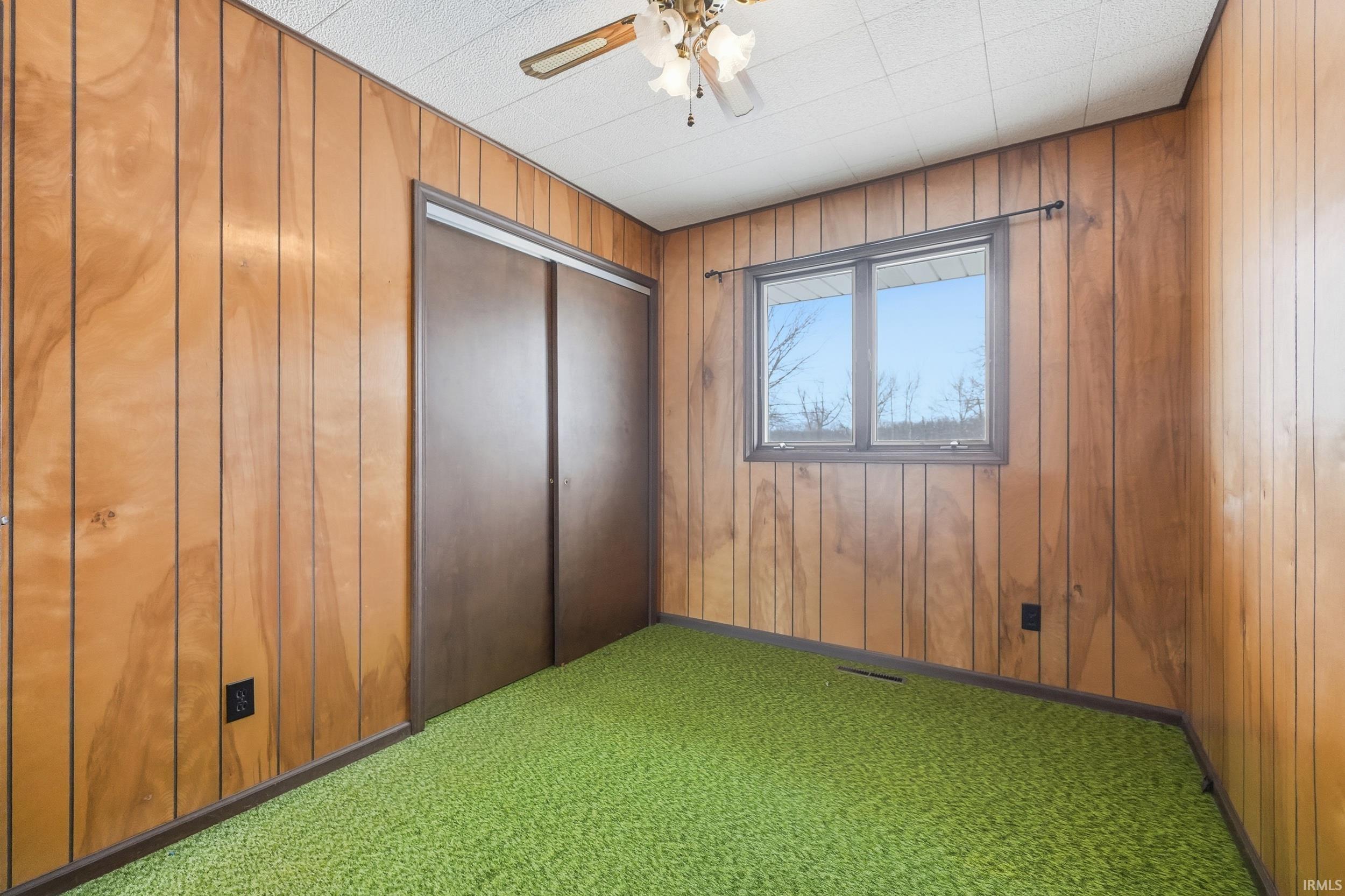Unfurnished bedroom with wooden walls, carpet flooring, ceiling fan, and a closet