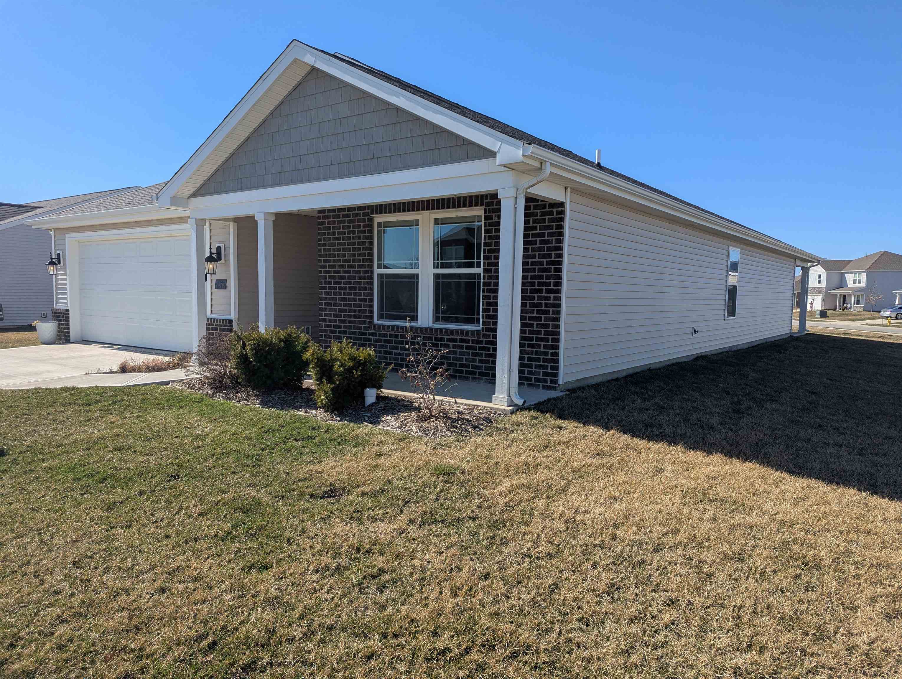 Ranch-style home with brick siding, a front lawn, a garage, covered porch, and driveway