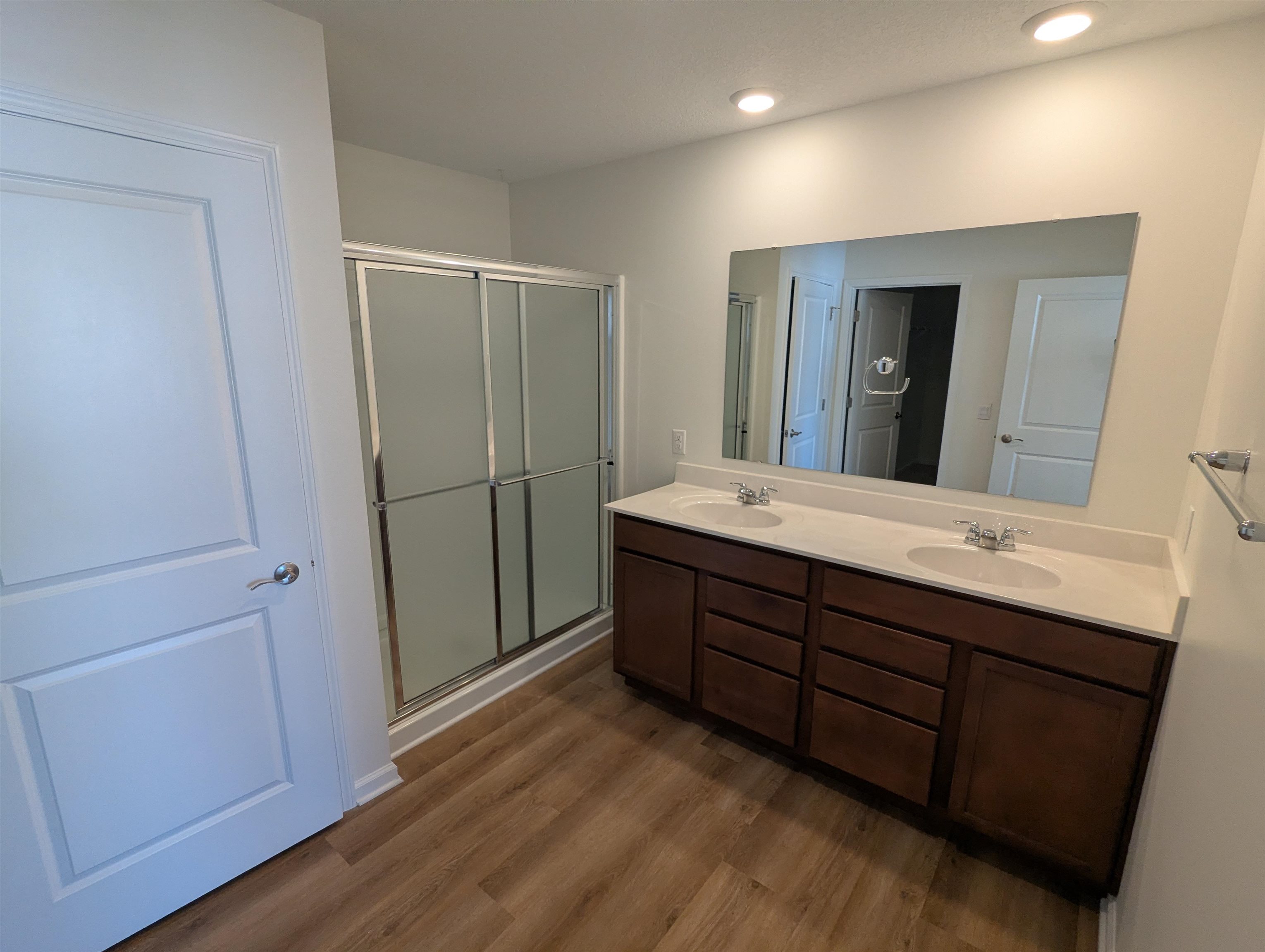 Full bathroom with double vanity, dark wood finished floors, and a stall shower
