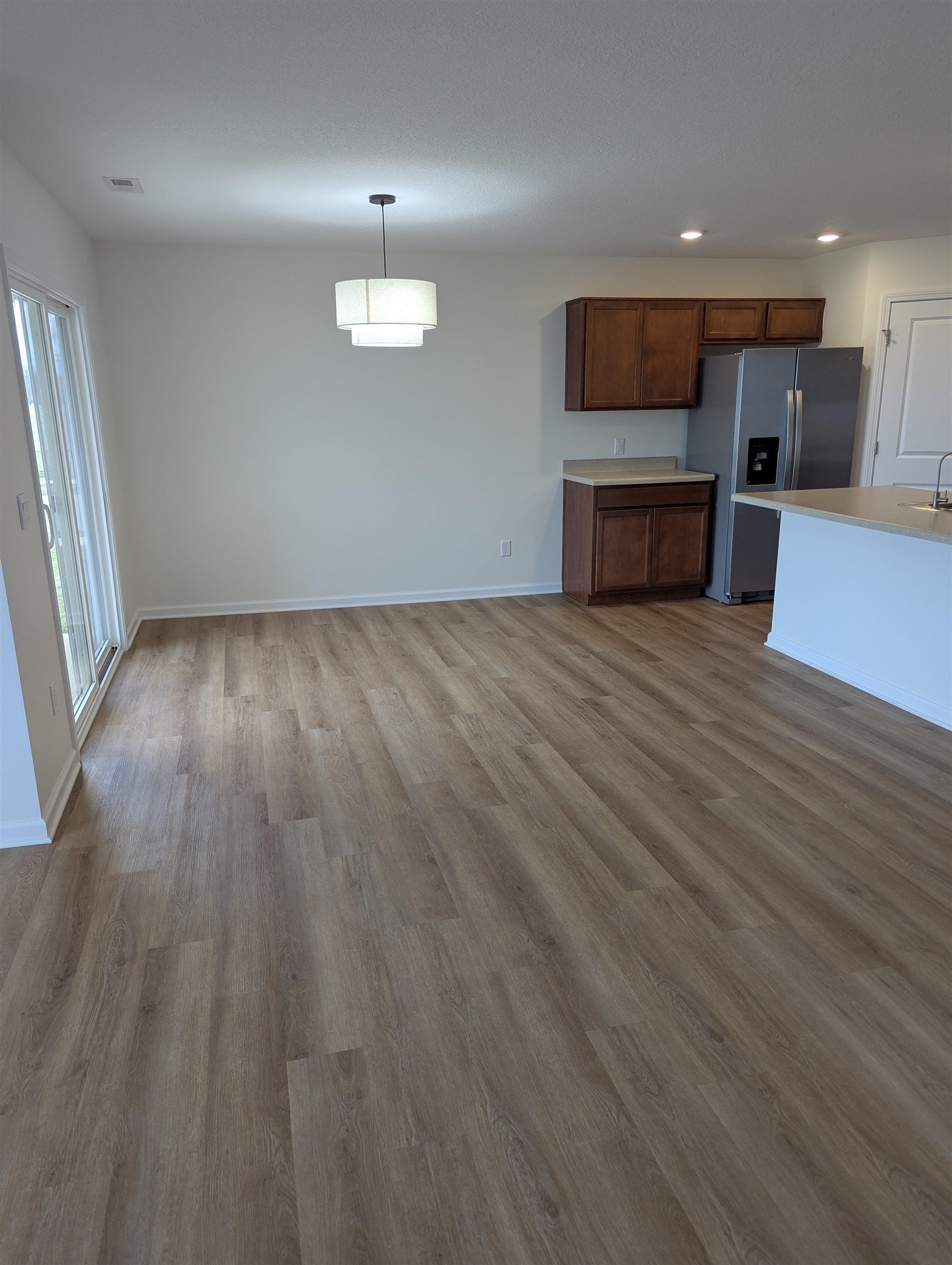 Kitchen featuring stainless steel fridge with ice dispenser, dark wood-type flooring, light countertops, wood finish cabinetry, and hanging light fixtures