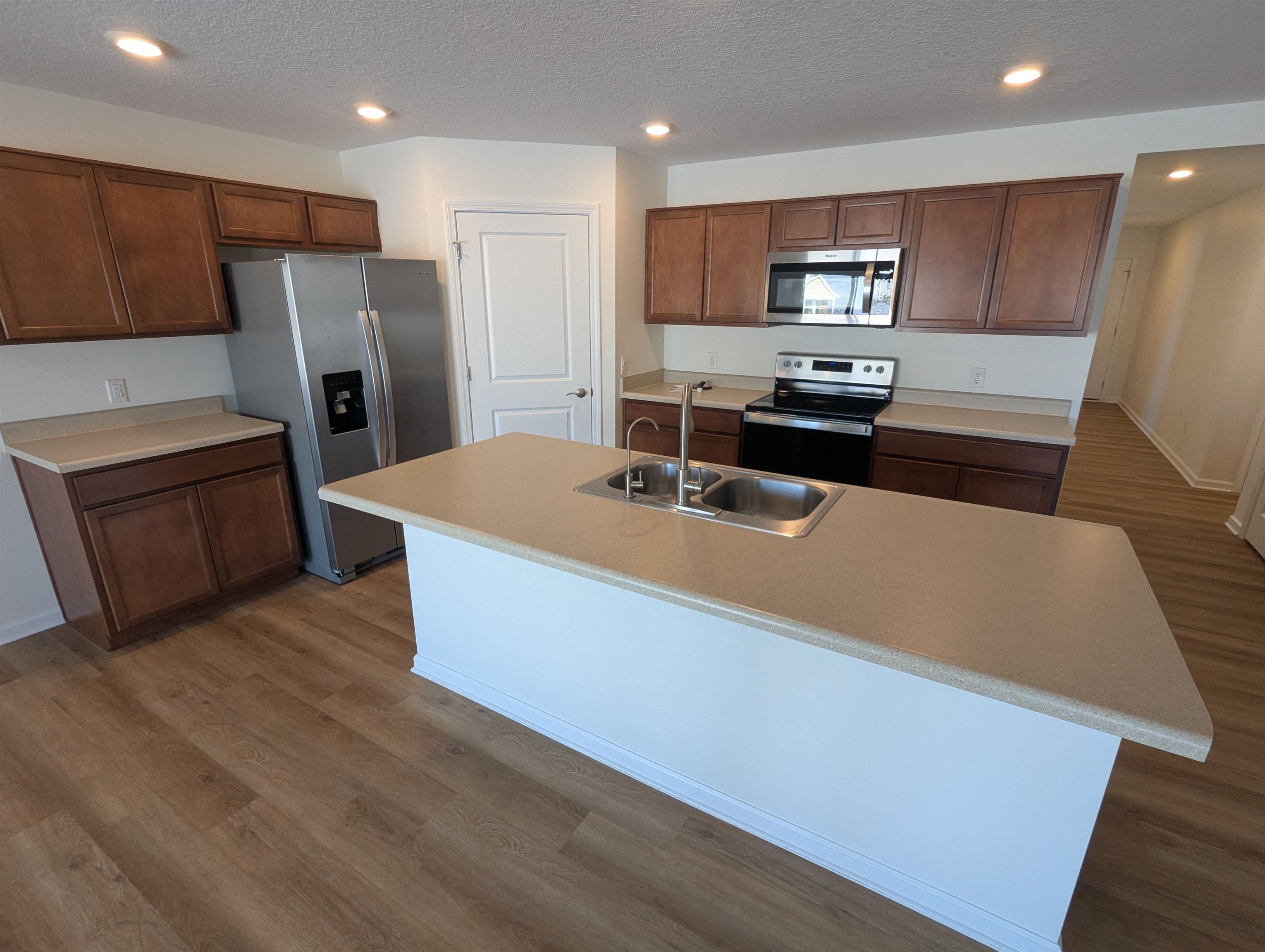 Kitchen featuring stainless steel appliances, a textured ceiling, light countertops, an island with sink, and recessed lighting