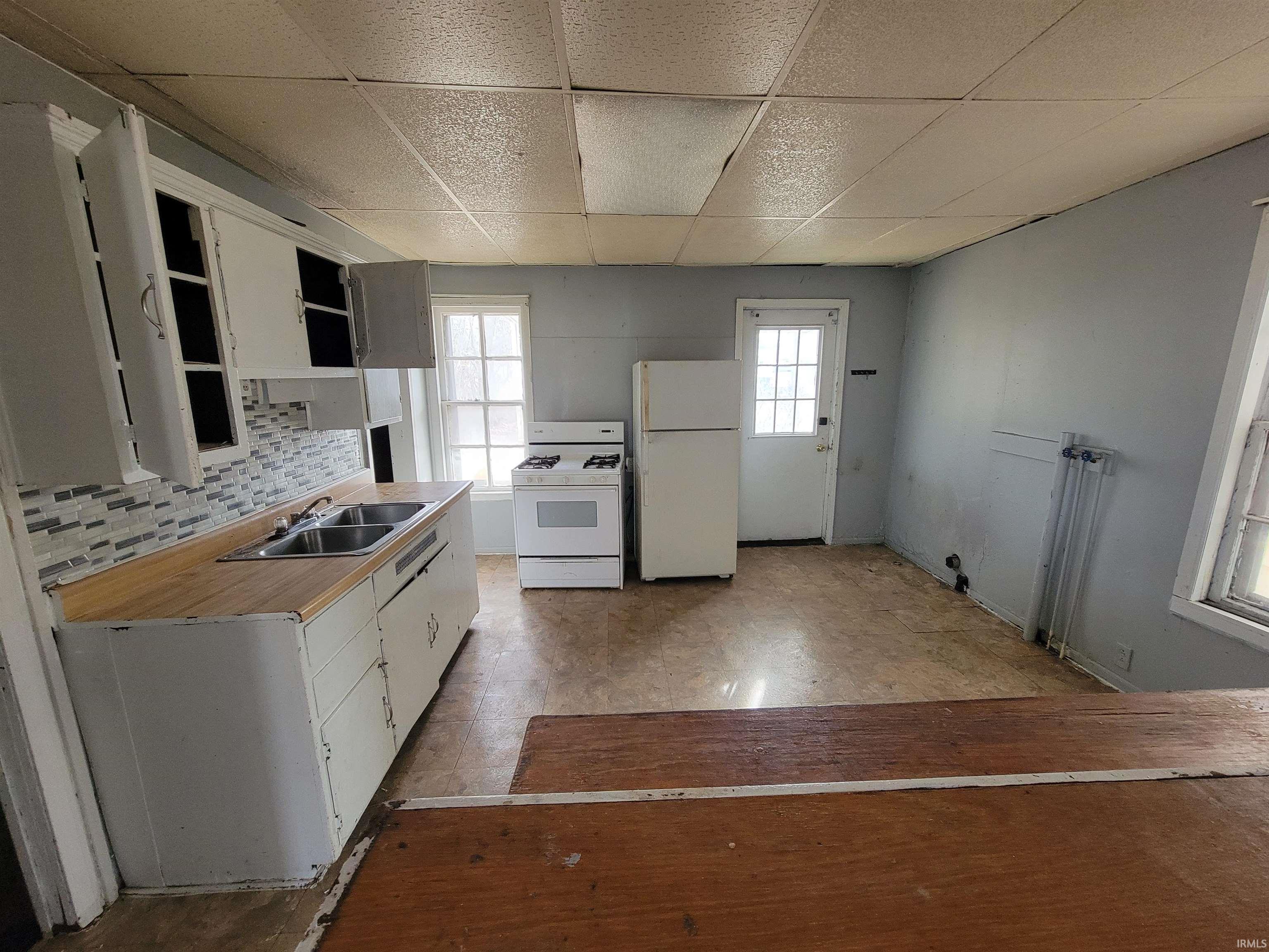 Kitchen with light countertops, a drop ceiling, white appliances, white cabinets, and open shelves