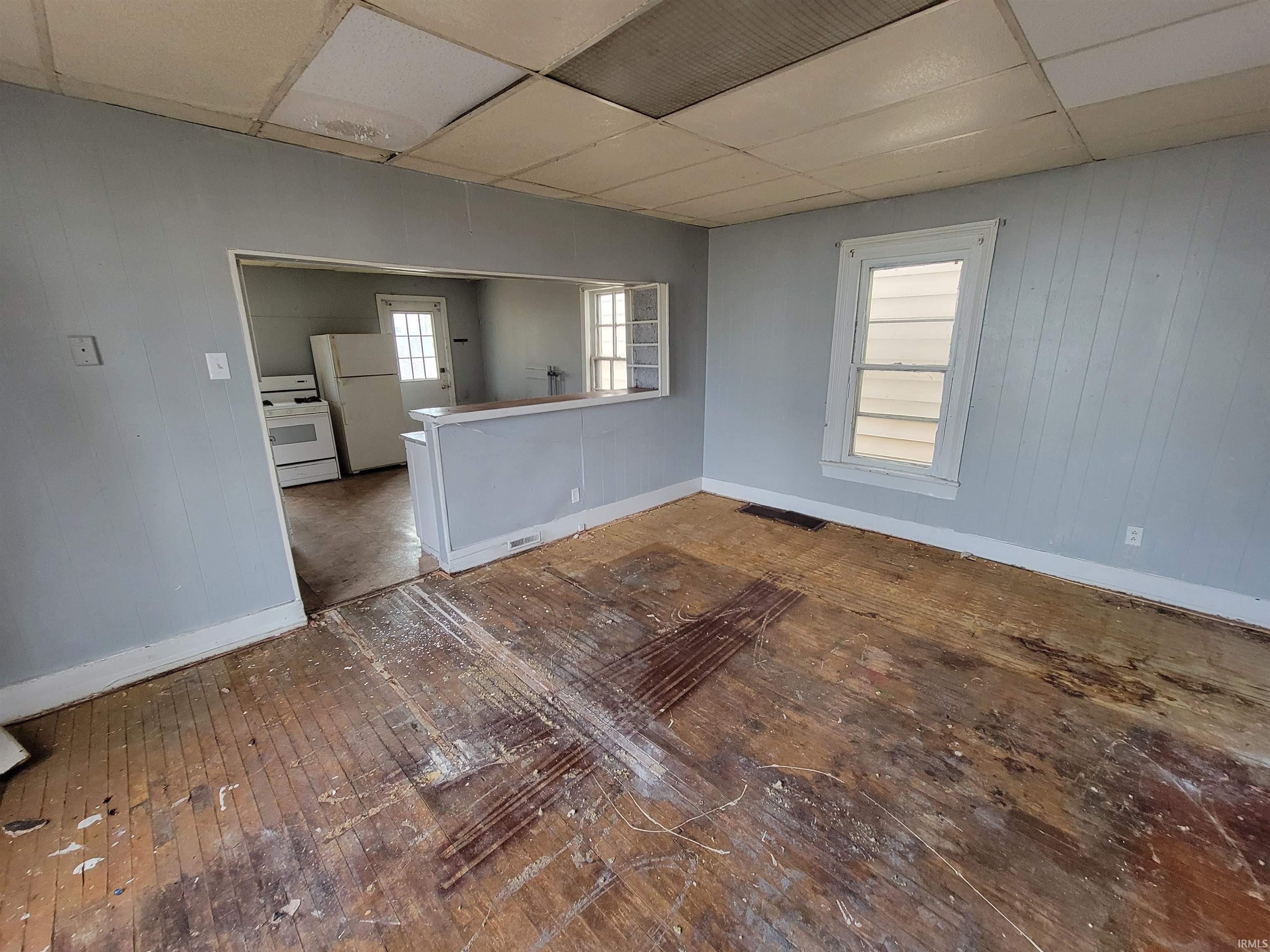 Unfurnished room featuring a drop ceiling and wooden walls
