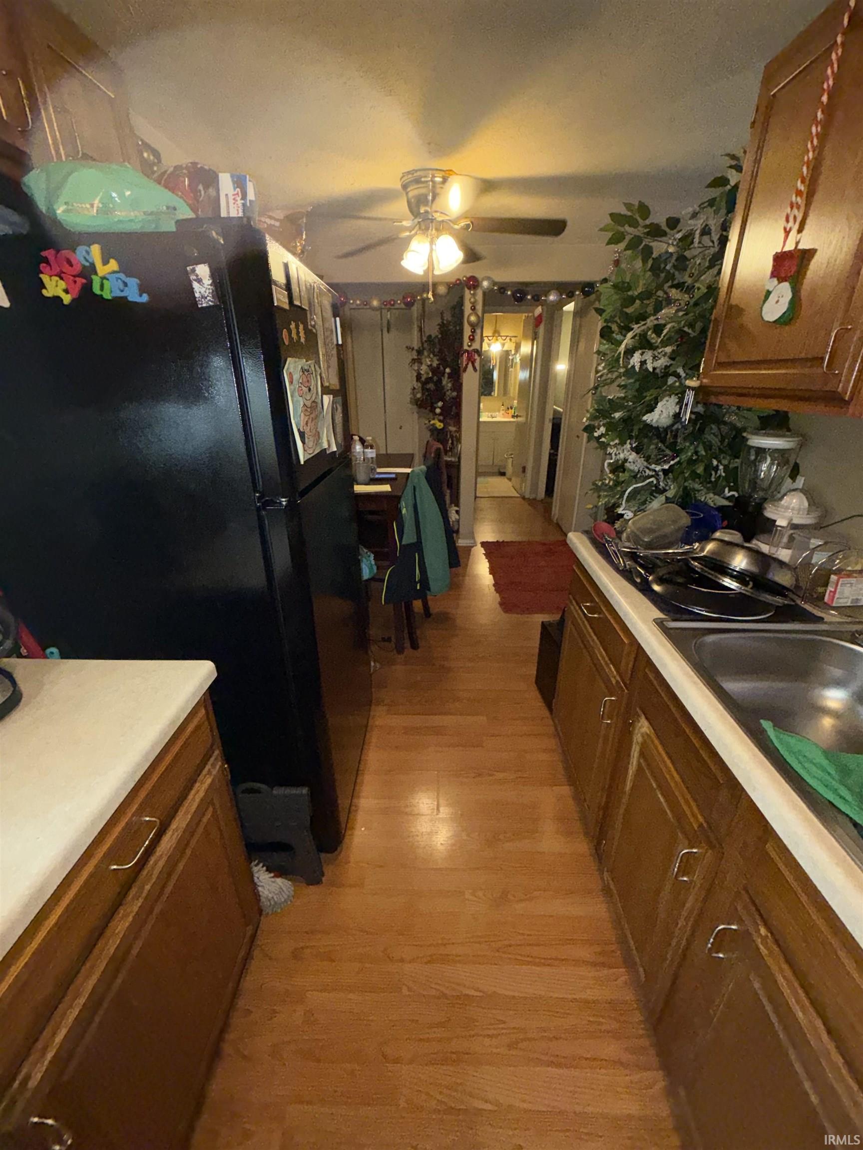 Kitchen featuring freestanding refrigerator, brown cabinetry, light wood-type flooring, a ceiling fan, and light countertops