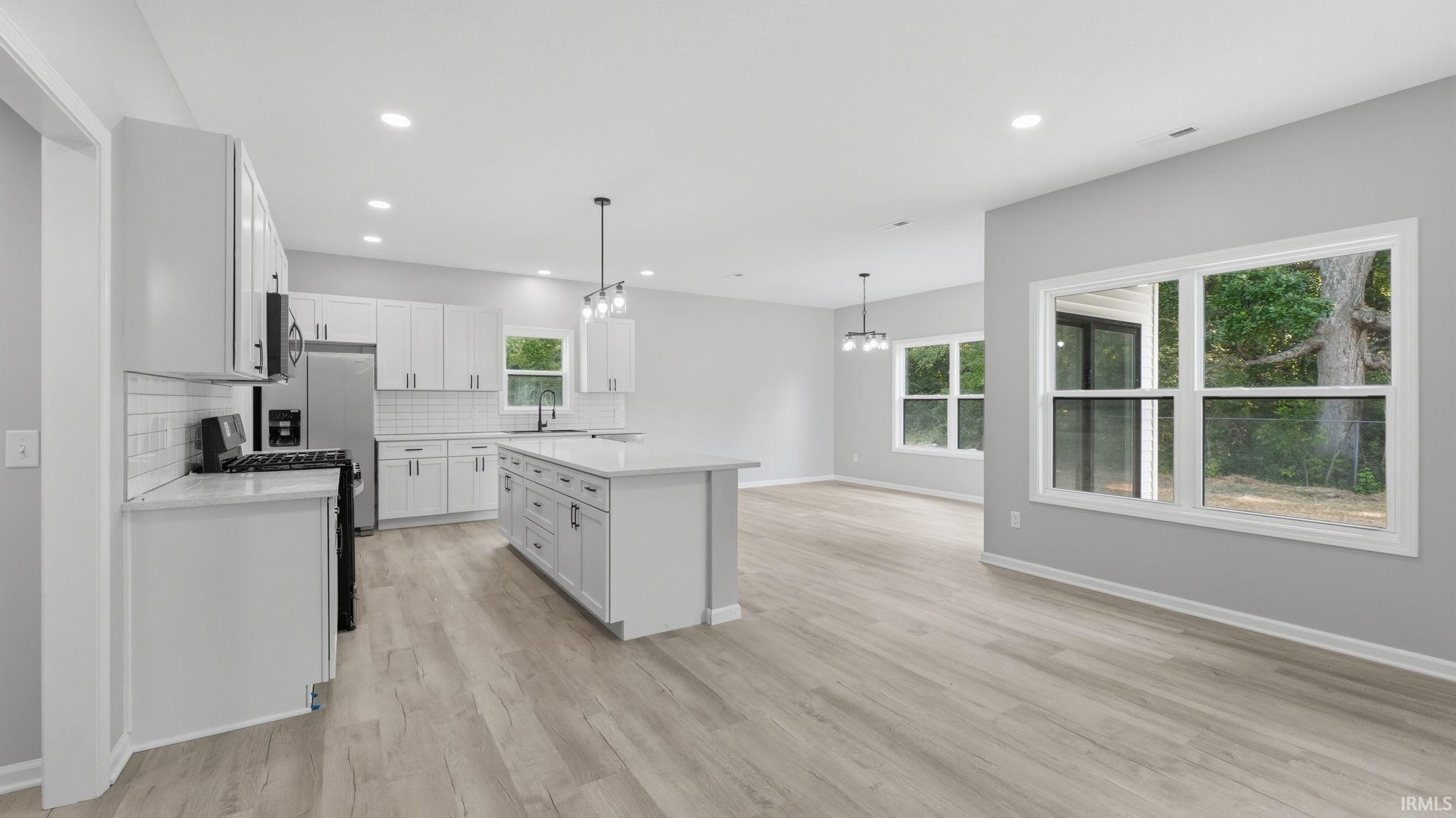Contemporary open-concept kitchen and living area featuring light wood-finish flooring, white cabinetry, a large kitchen island with a white countertop, and recessed lighting