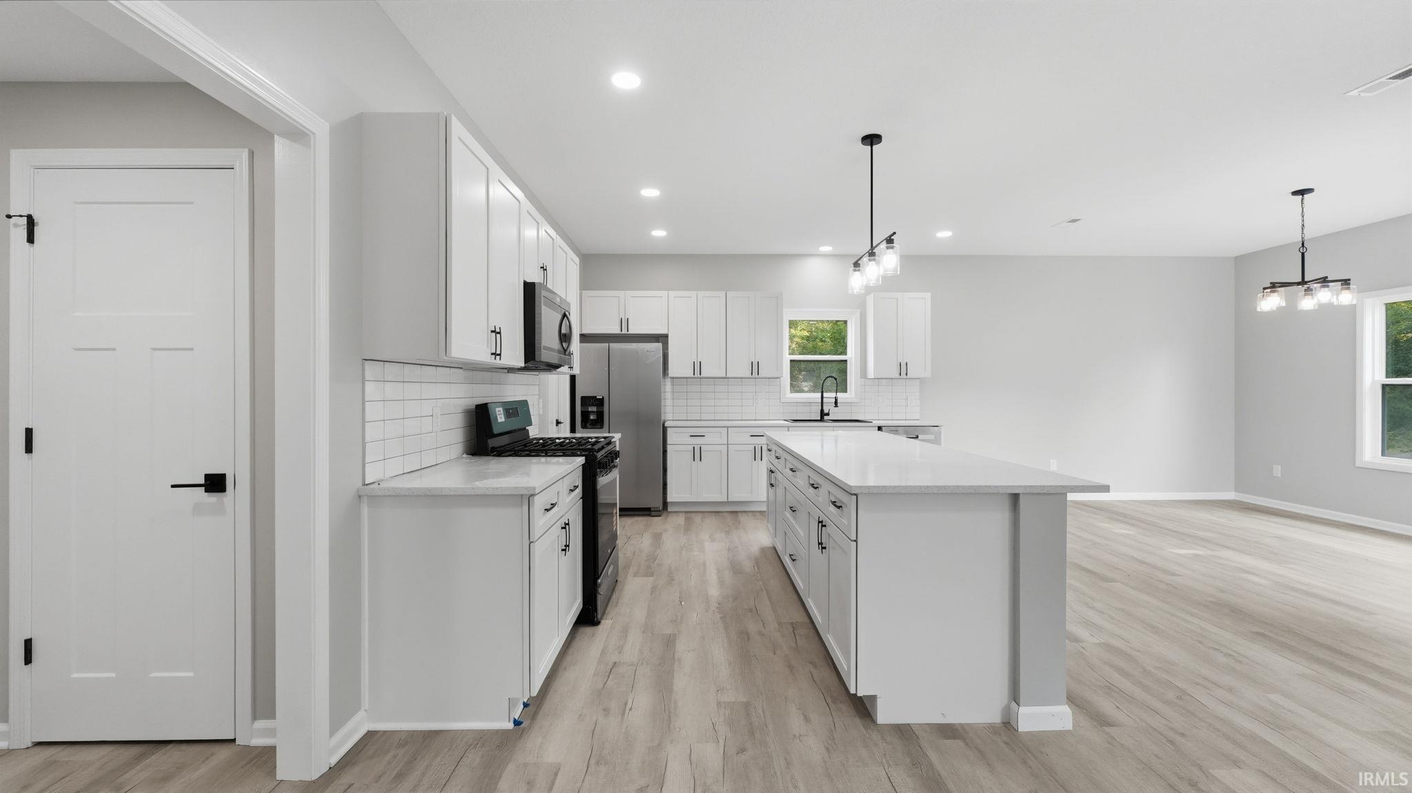 Contemporary kitchen featuring white cabinetry, a large center island, black appliances, subway tile backsplash, and light wood-finish flooring