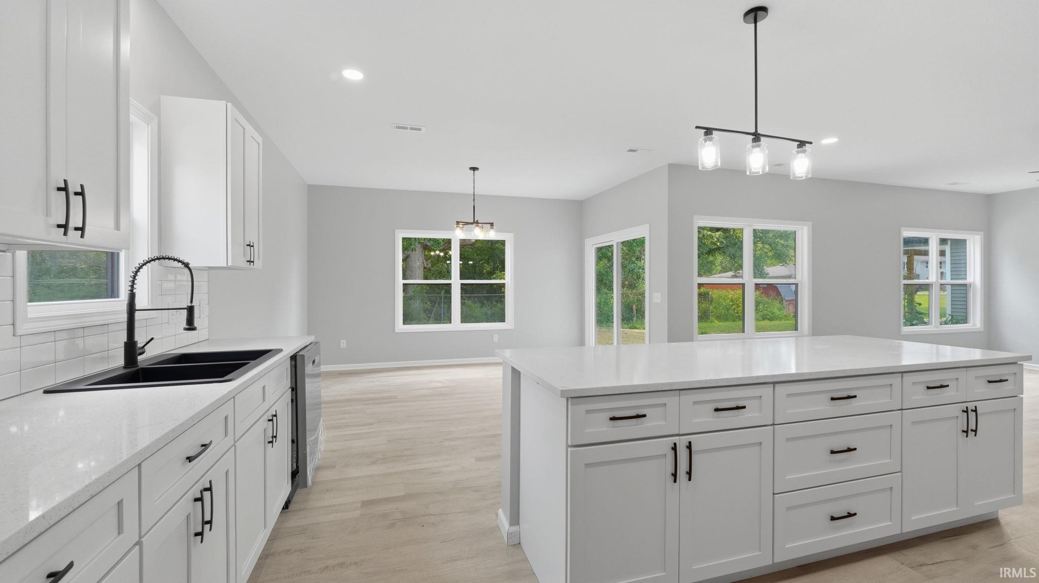Modern kitchen featuring white shaker cabinetry with matte black hardware, stone-finish countertops, a black double-basin sink, and wood-finish flooring