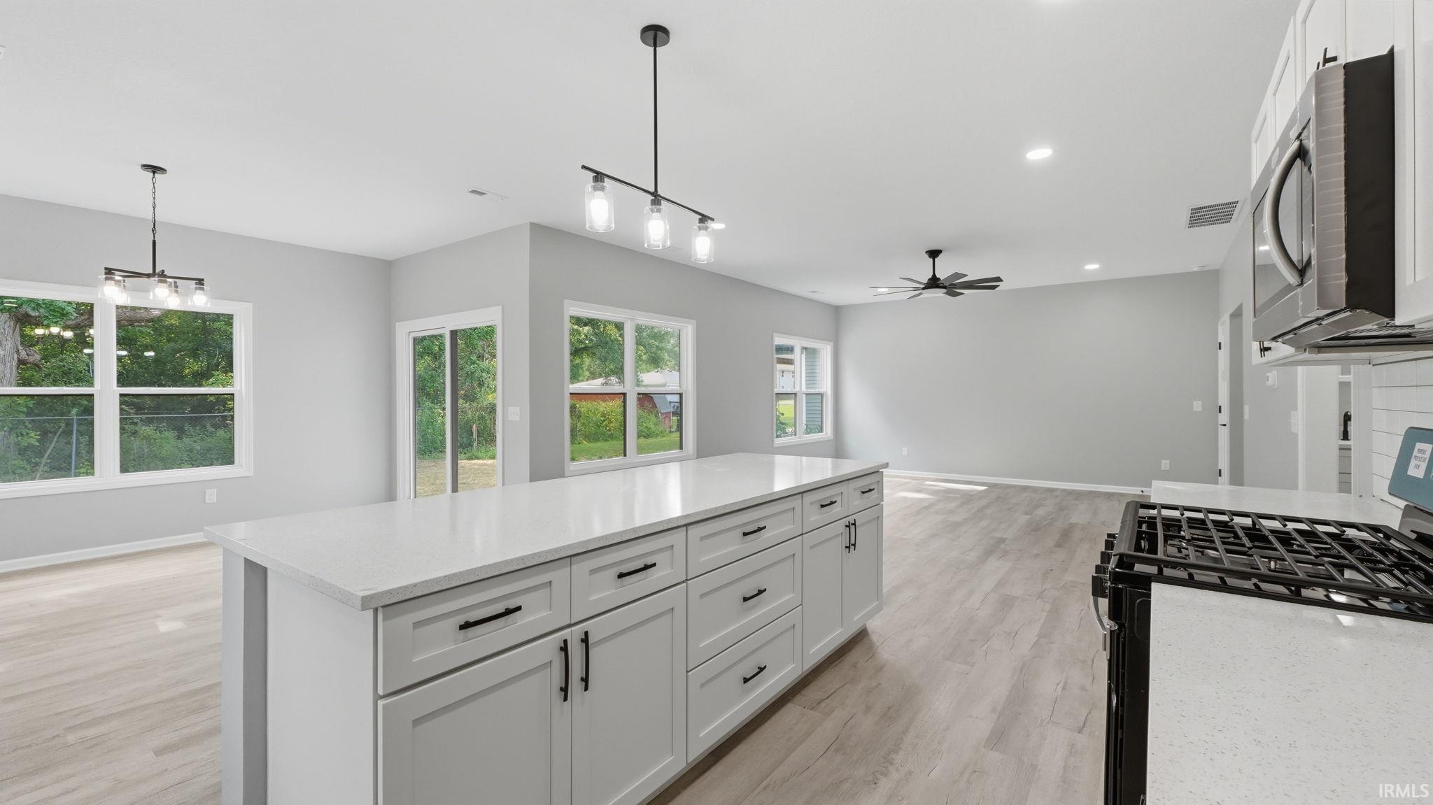 Open-concept kitchen featuring a large central island with white cabinetry and a light-toned countertop, stainless steel gas range, and recessed lighting