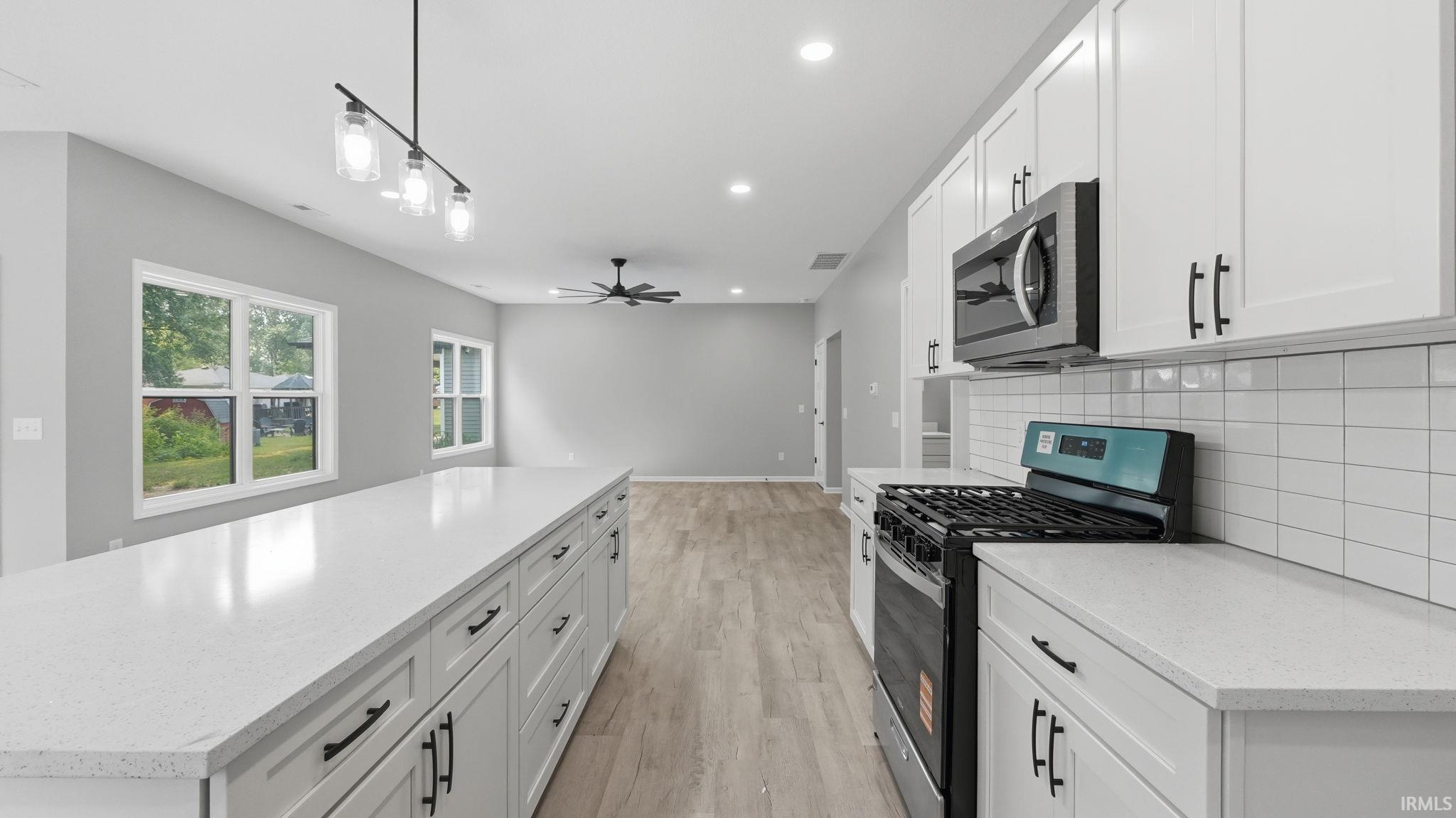 Modern kitchen featuring an expansive center island with white countertops, white shaker-style cabinetry with matte black hardware, stainless steel appliances, and a white subway tile backsplash