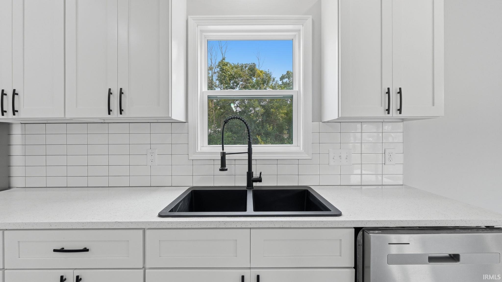 Kitchen featuring a black double basin sink with a gooseneck faucet, white shaker-style cabinetry, light speckled countertops, a horizontal subway tile backsplash, and a stainless steel dishwasher