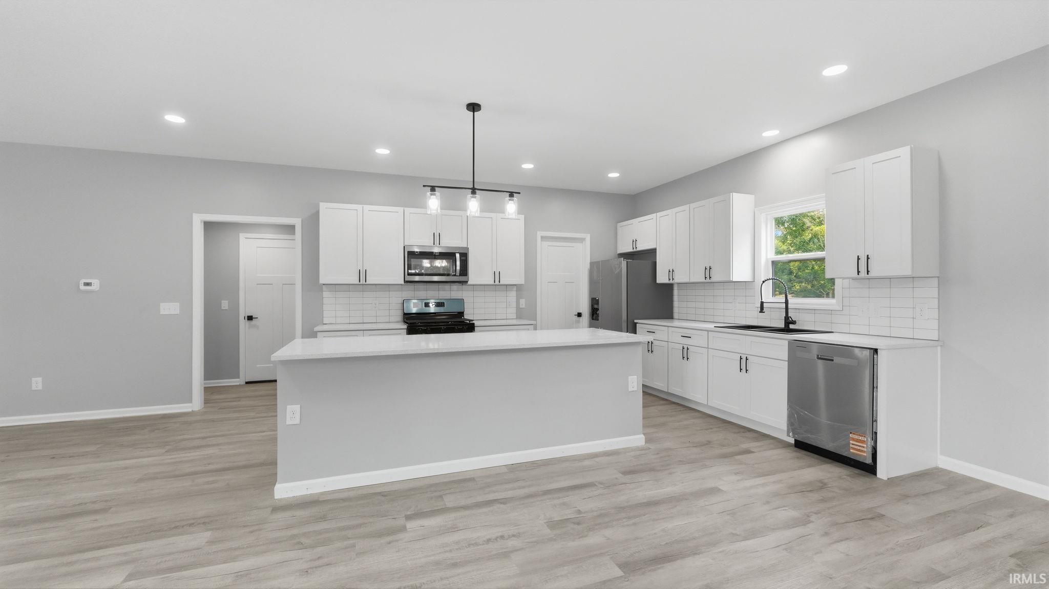 Modern kitchen featuring a central island, white cabinetry, integrated stainless steel appliances, and wood-finish flooring