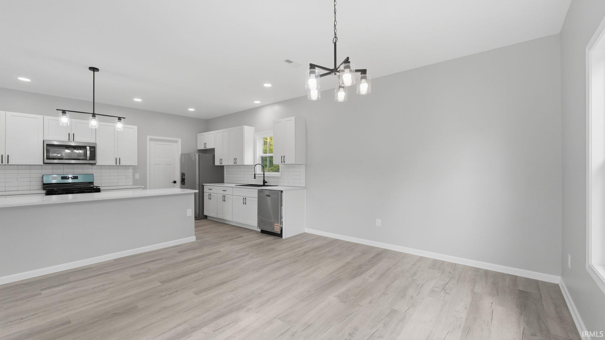 Open-concept kitchen and dining area featuring light wood-finish flooring, white cabinetry, stainless steel appliances, and a subway tile backsplash