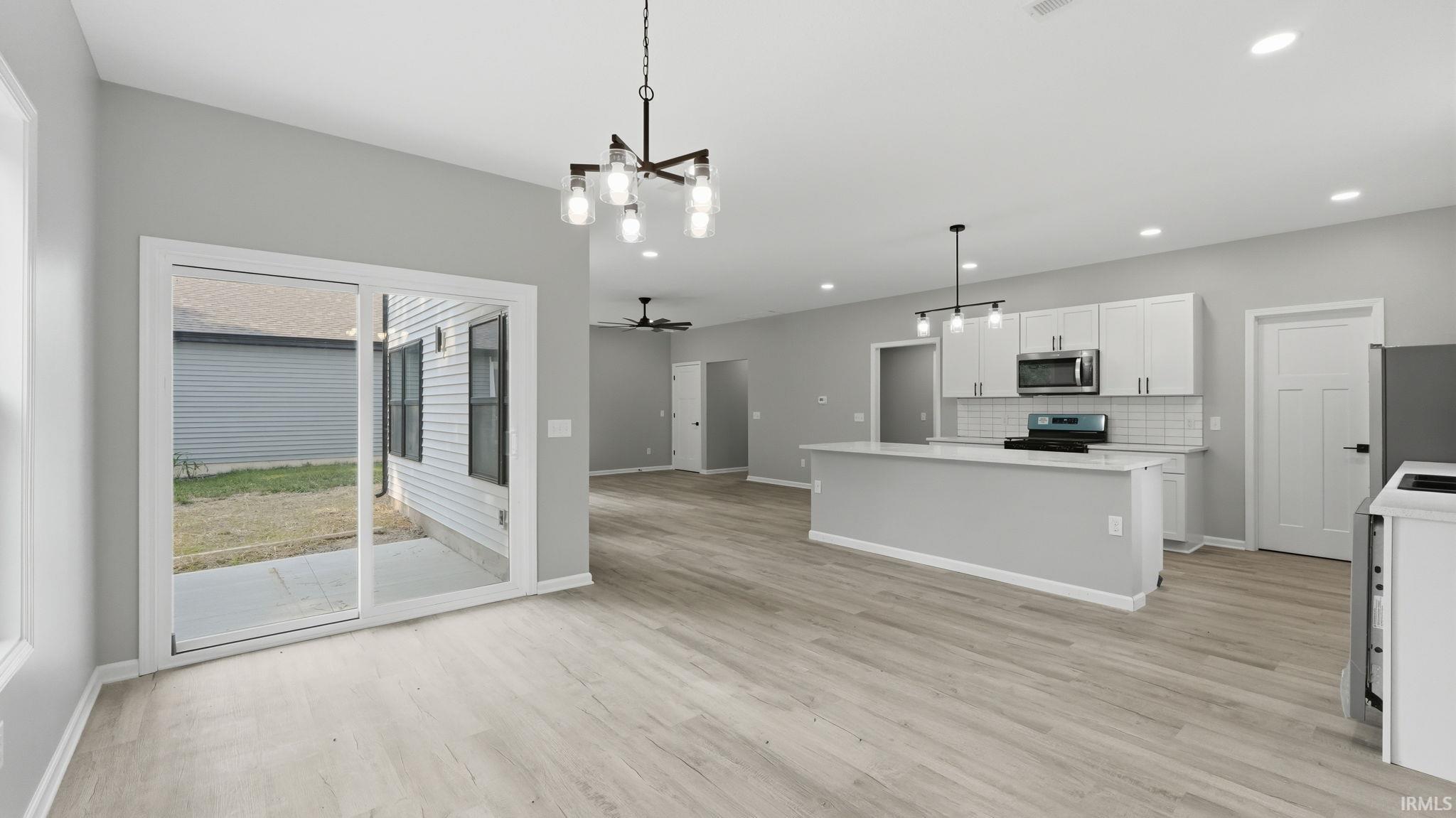 Open-concept living space featuring wood-finish flooring, a modern kitchen island with pendant lighting, white shaker cabinetry, stainless steel appliances, and a subway tile backsplash