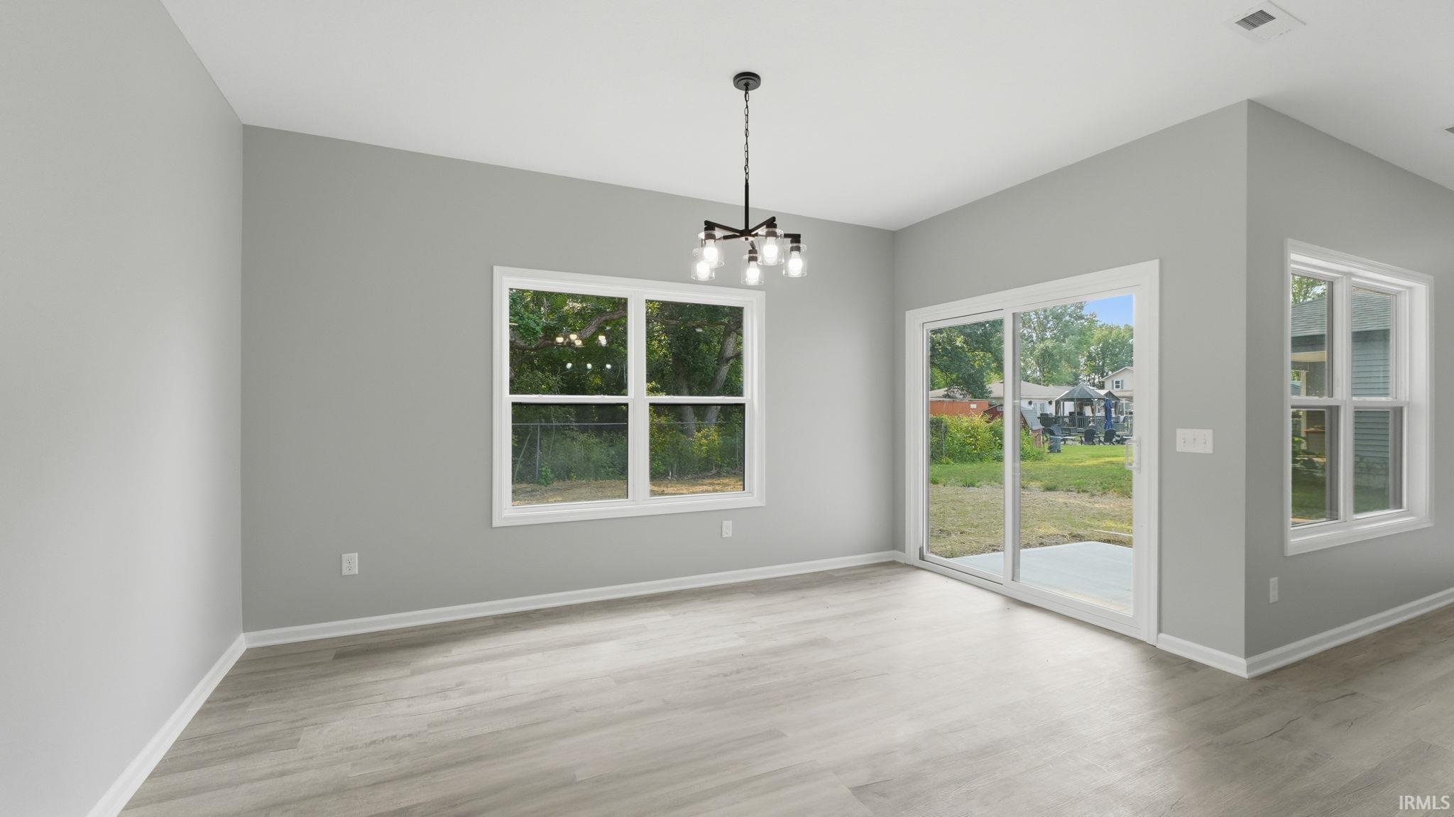 Open-concept living area featuring light gray walls, wood-finish flooring, and a contemporary chandelier
