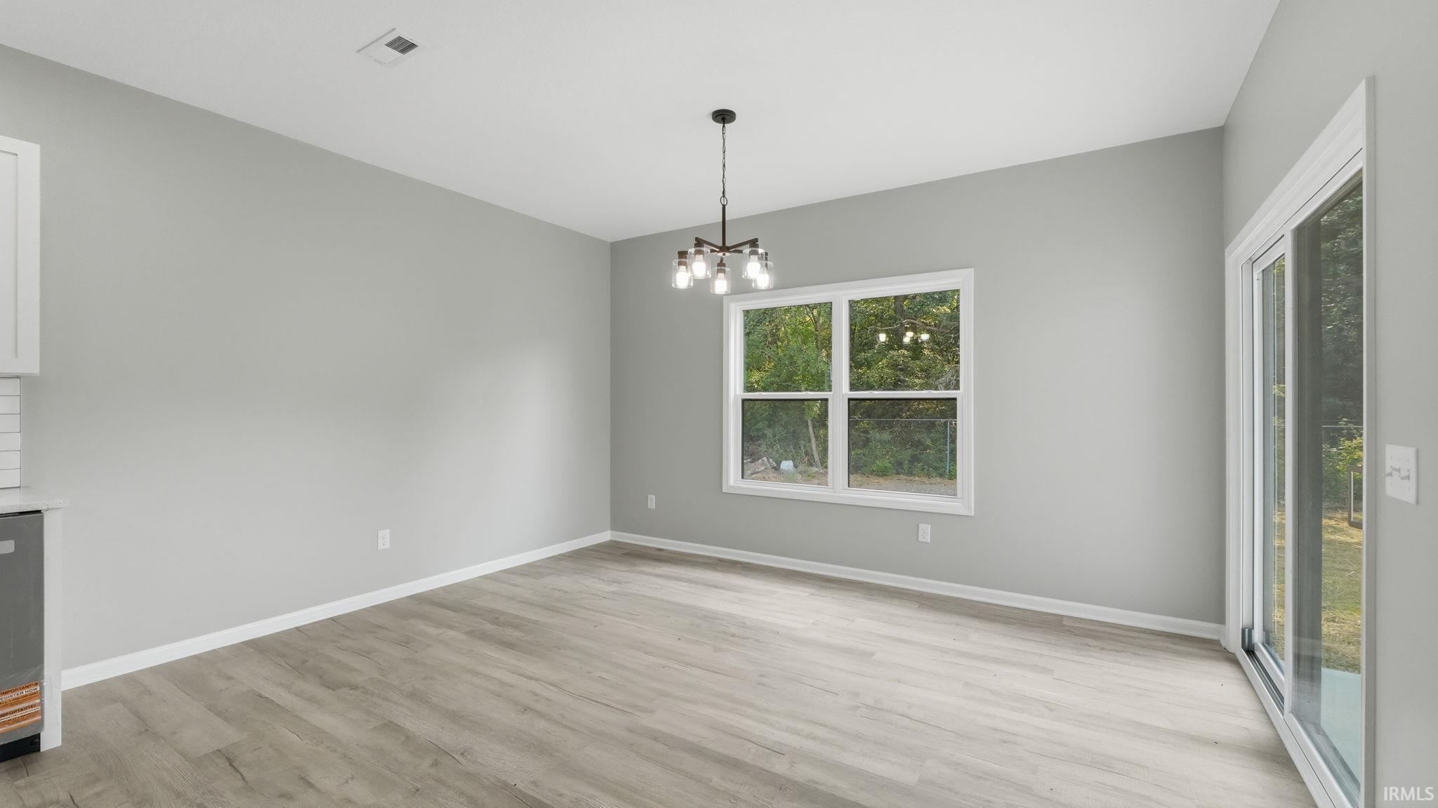 Spacious room featuring light gray walls, wood-finish flooring, and a contemporary black chandelier