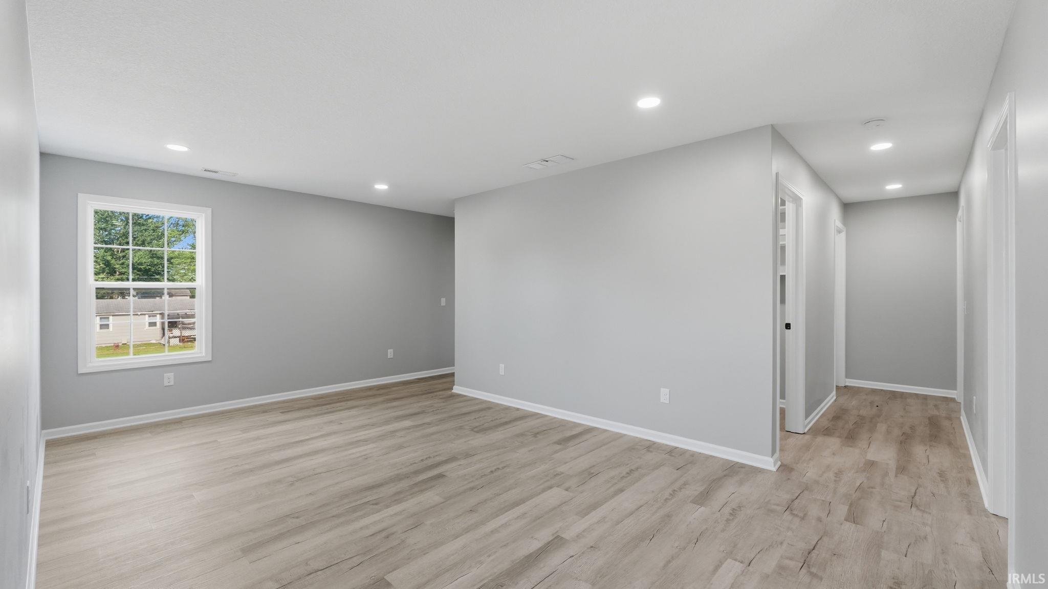 Open concept living area featuring wood-finish flooring, recessed lighting, neutral paint tones, white trim, and a window offering exterior views